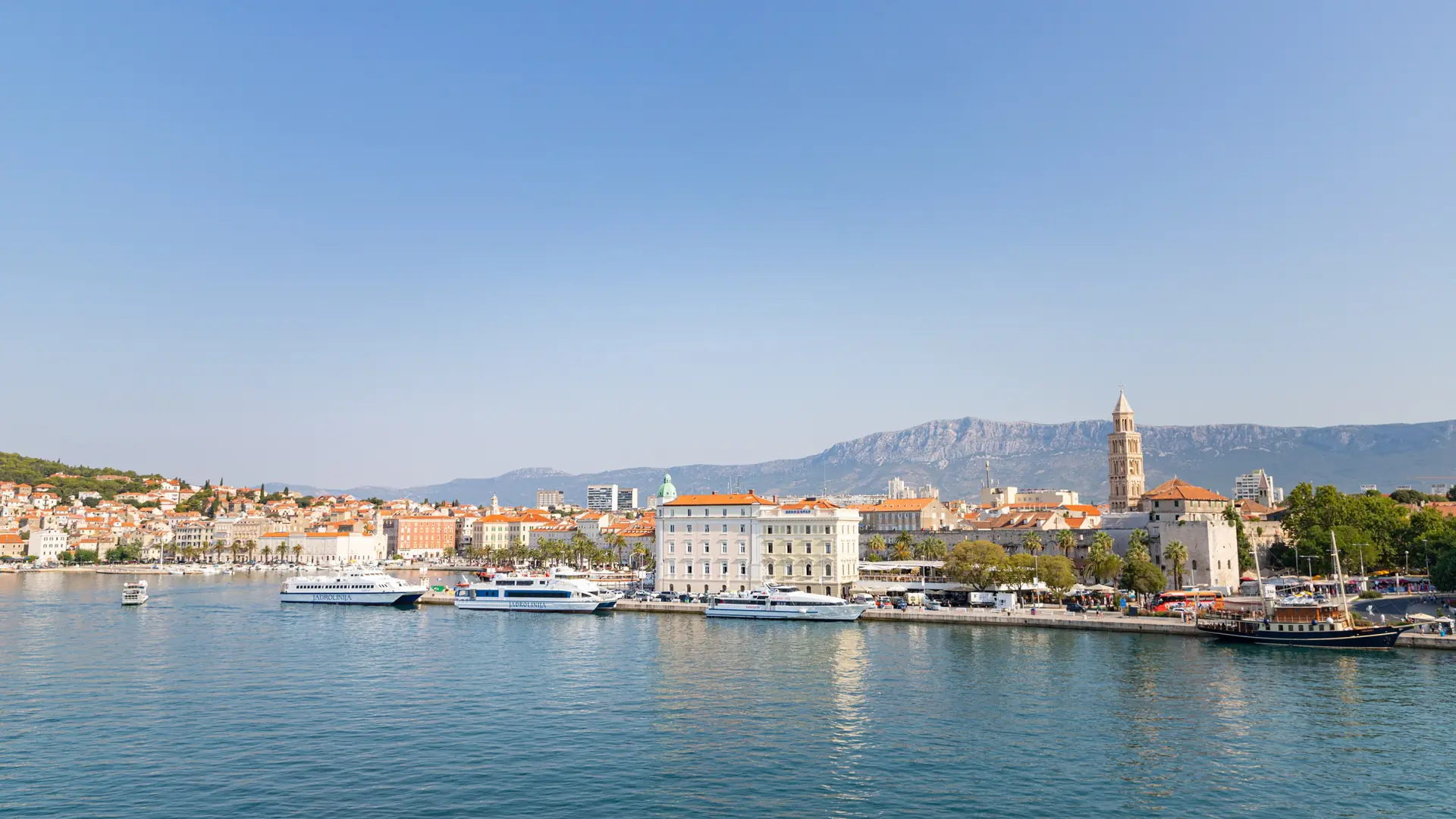 Jadrolinija ferries moored in Split harbour beneath the cathedral bell tower on a bright day