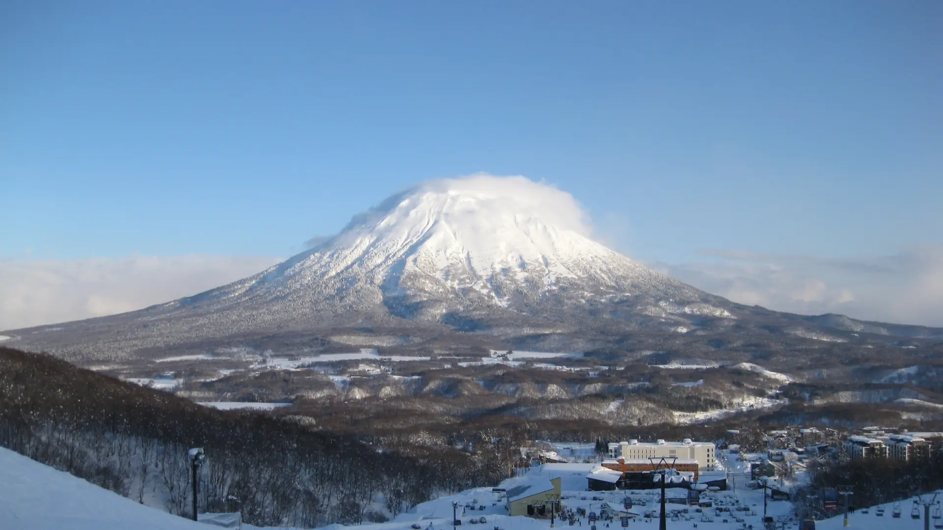 Snow-covered Mount Yotei above Niseko’s winter slopes and village in sunshine