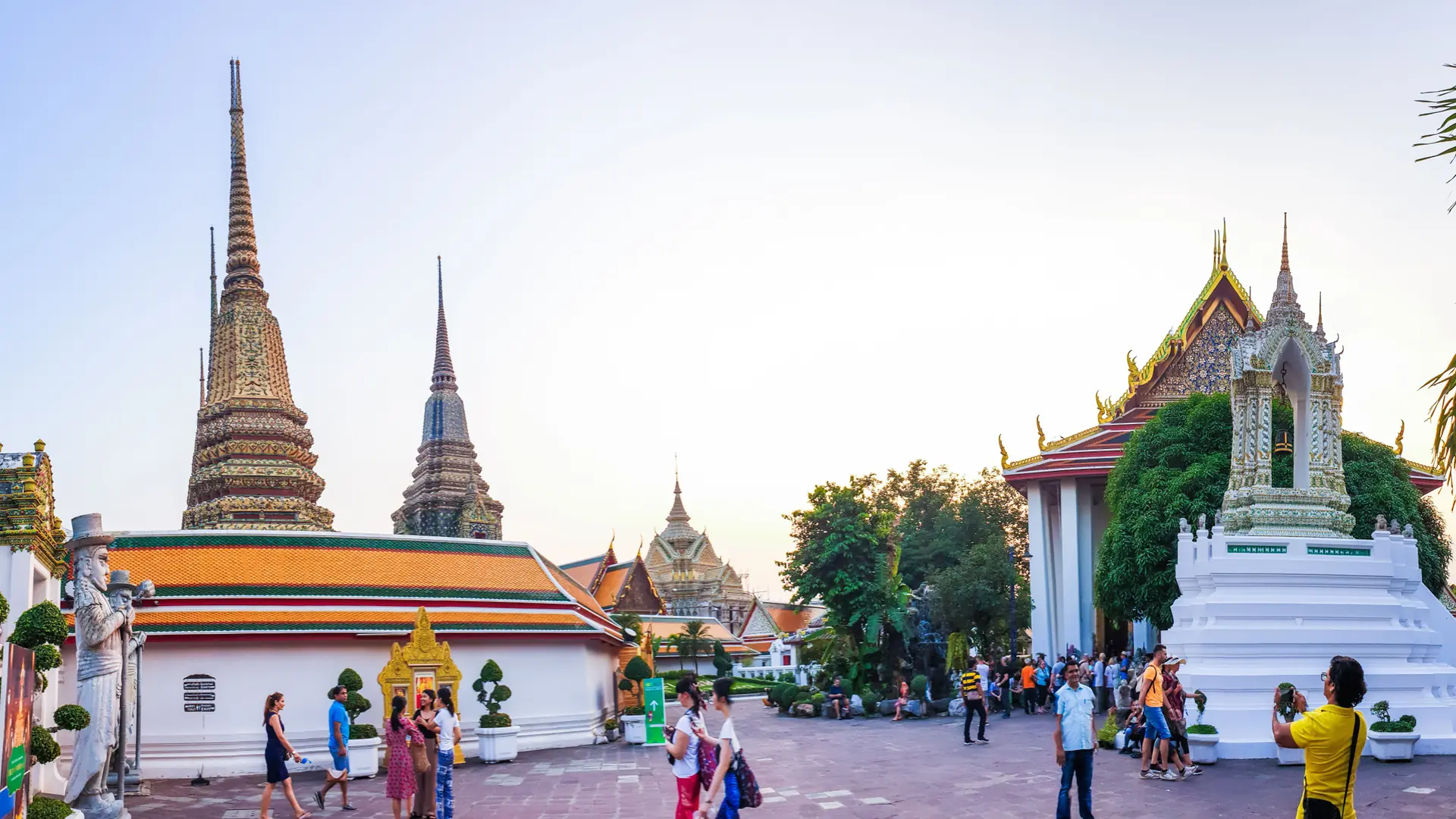 Visitors walking among the gilded roofs and chedis of Wat Pho in Bangkok