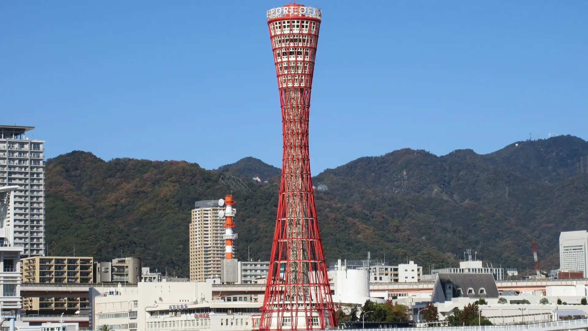 Kobe Port Tower, bright waterfront and blue harbour framed by the Rokko Mountains on a clear day
