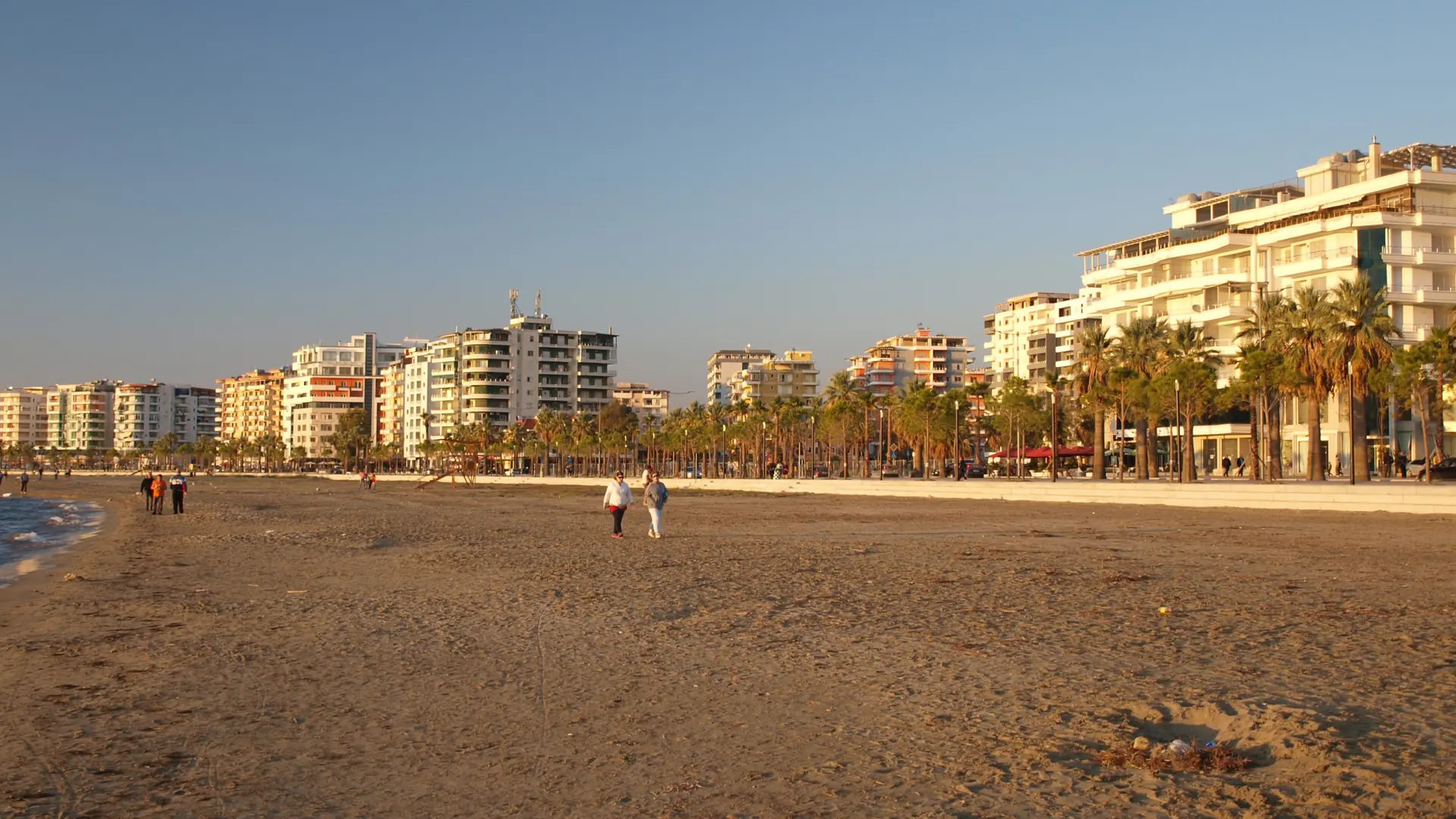 The sandy city beach and seafront apartment blocks along Vlorë's Lungomare in warm late-afternoon sun