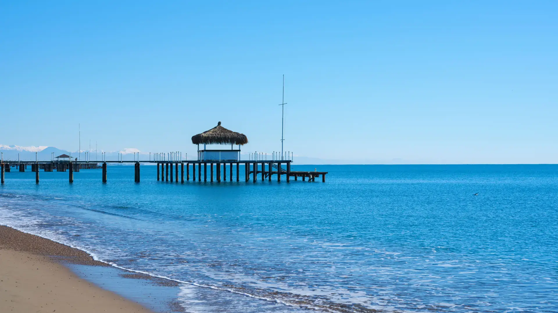 Sunny sandy resort beach with a long pier reaching into turquoise water