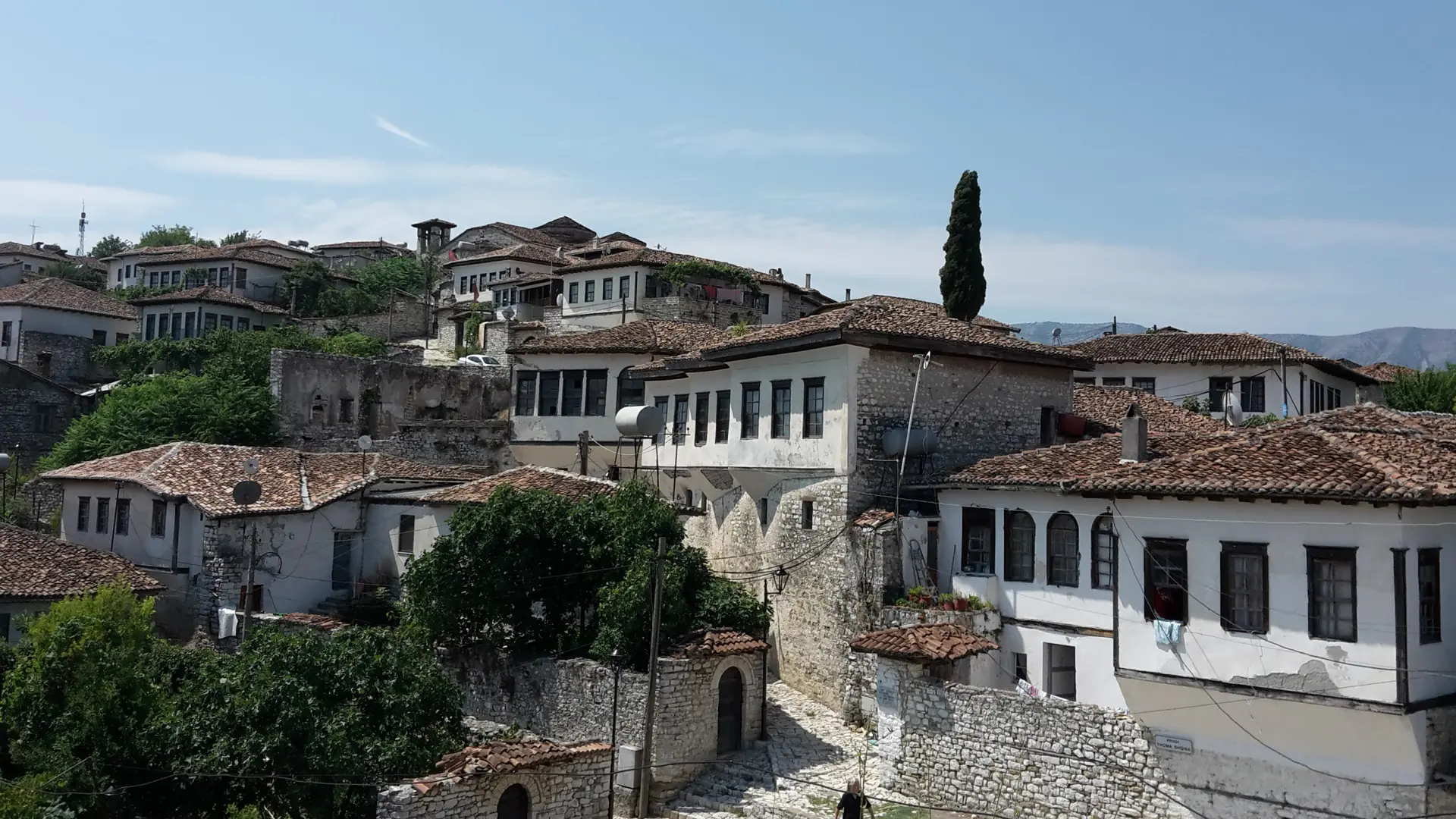 Stone houses with tiled roofs inside the walls of Berat Castle under a clear blue sky