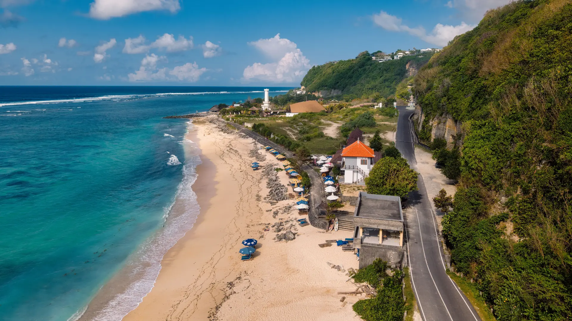 Turquoise water and a sandy Bali beach below limestone cliffs and a white lighthouse