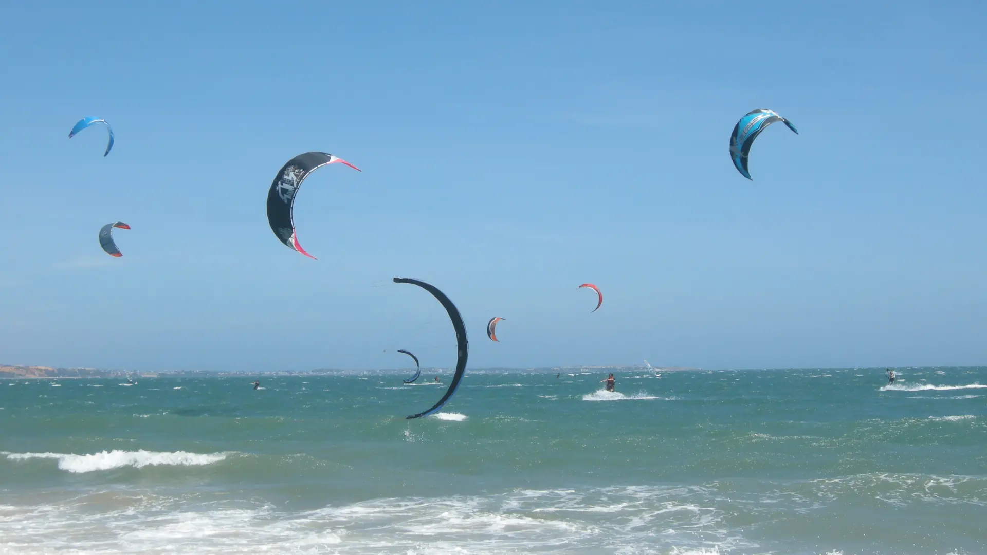 Kitesurfers over turquoise water off Mui Ne beach beneath a blue sky