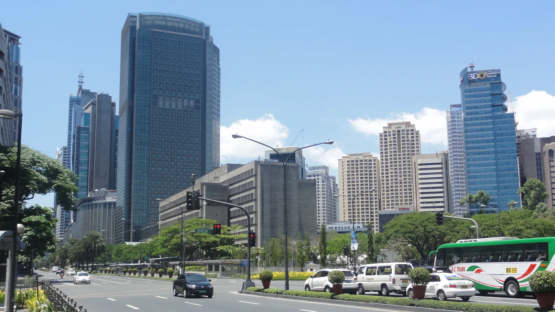 Office towers and trees along Ayala Avenue in Makati under a clear blue sky