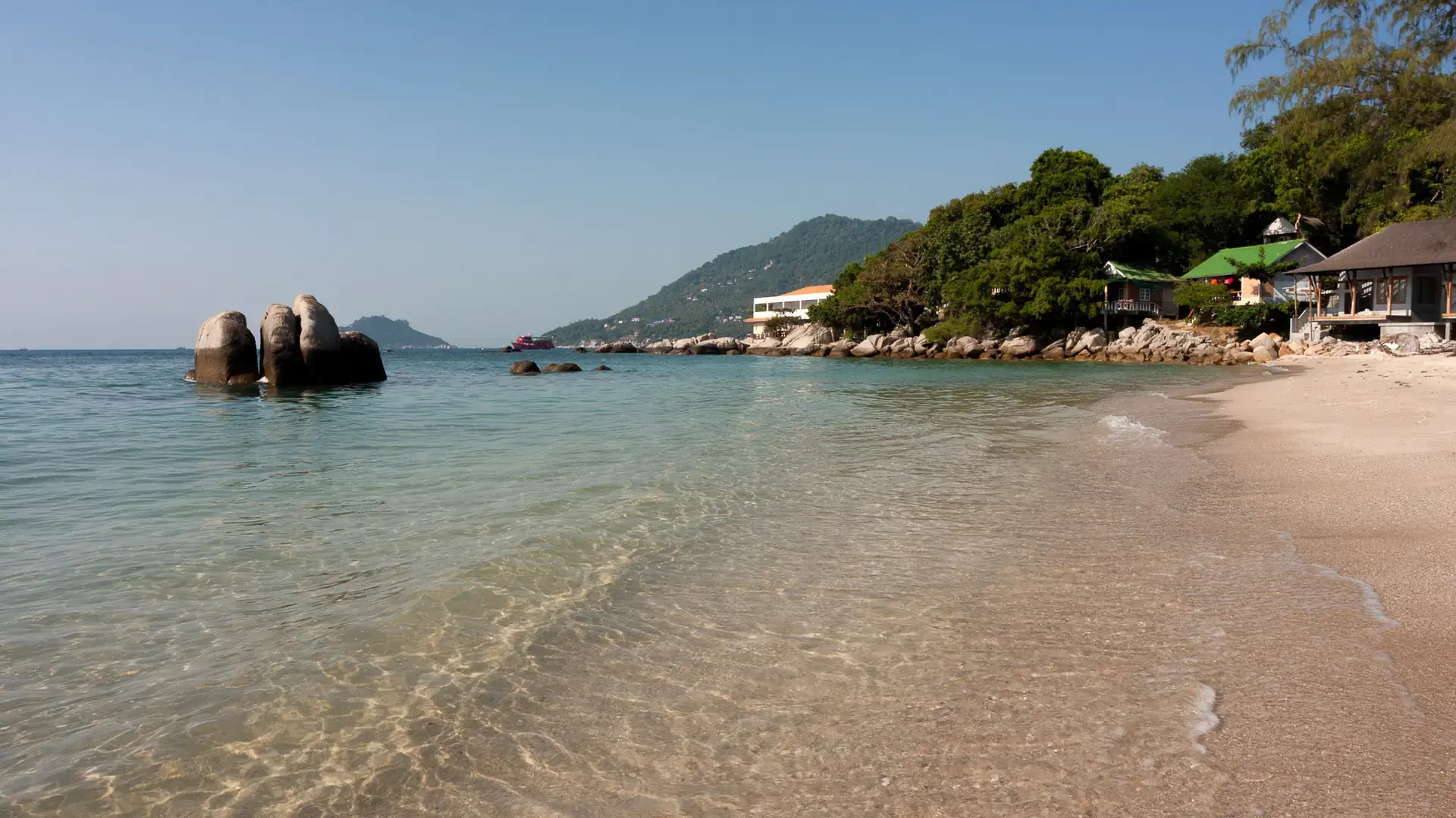 Sunny sand and granite boulders beside blue water on wider Koh Tao