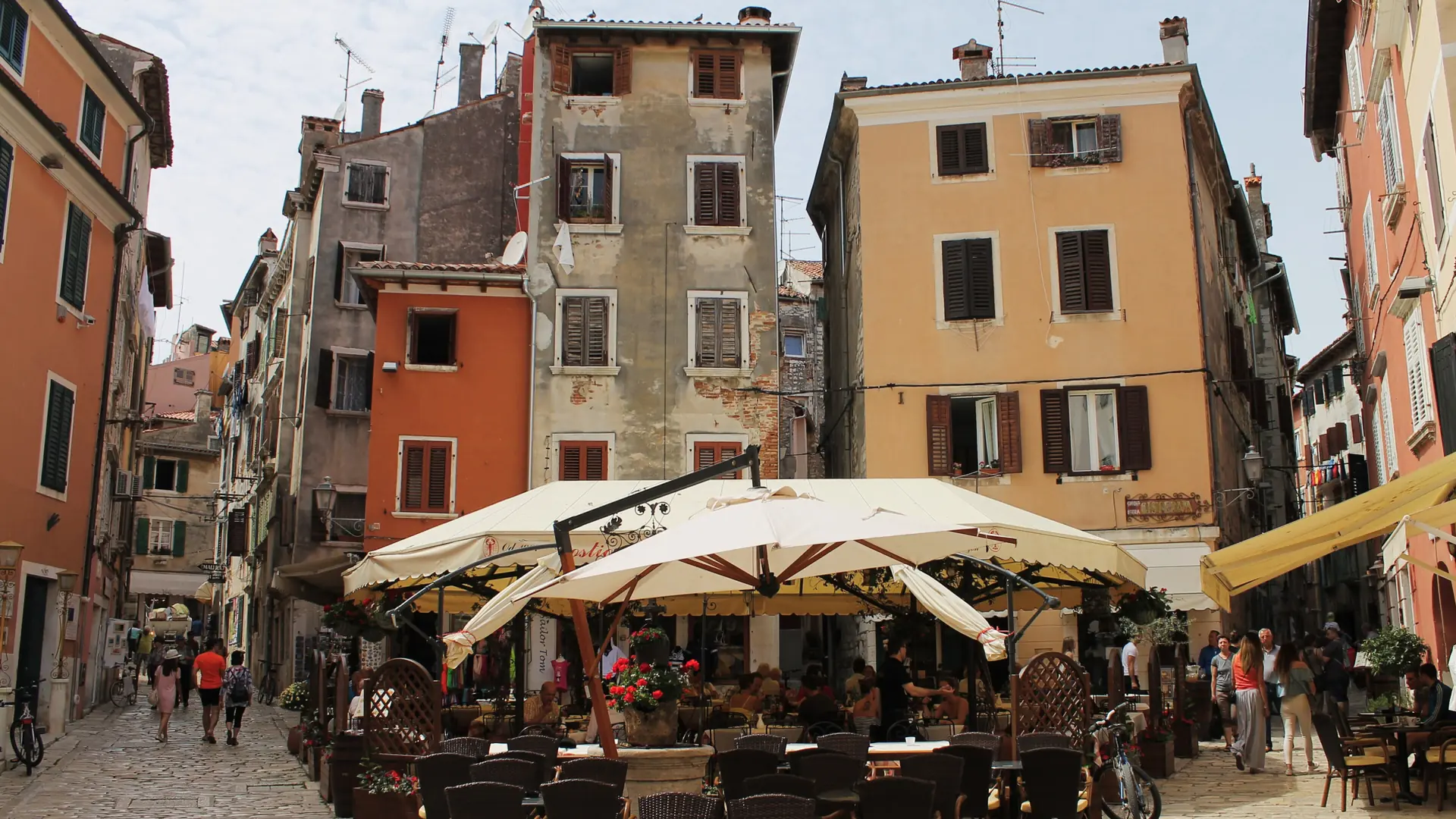 A sunlit cafe square on cobblestones between colourful old-town houses in Rovinj
