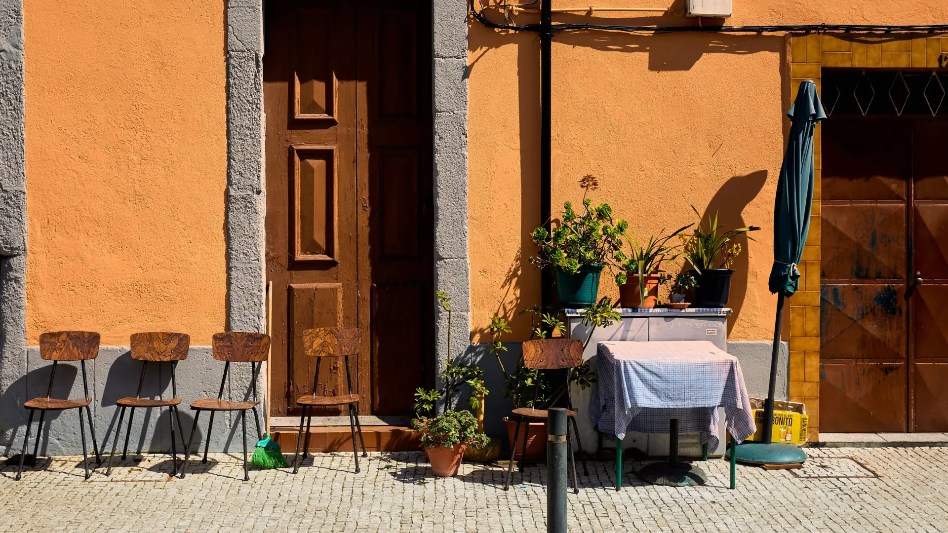 a sunlit vivid orange façade with a wooden door and café tables in Funchal's old town