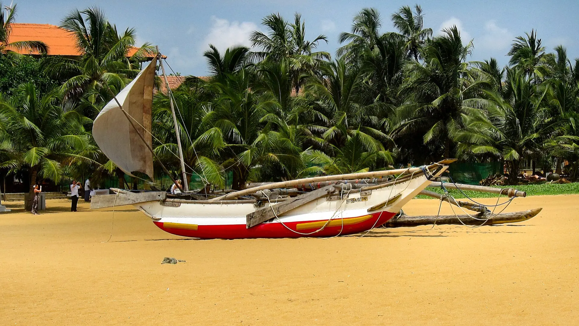 Traditional fishing boat with its sail raised on sunny Negombo Beach