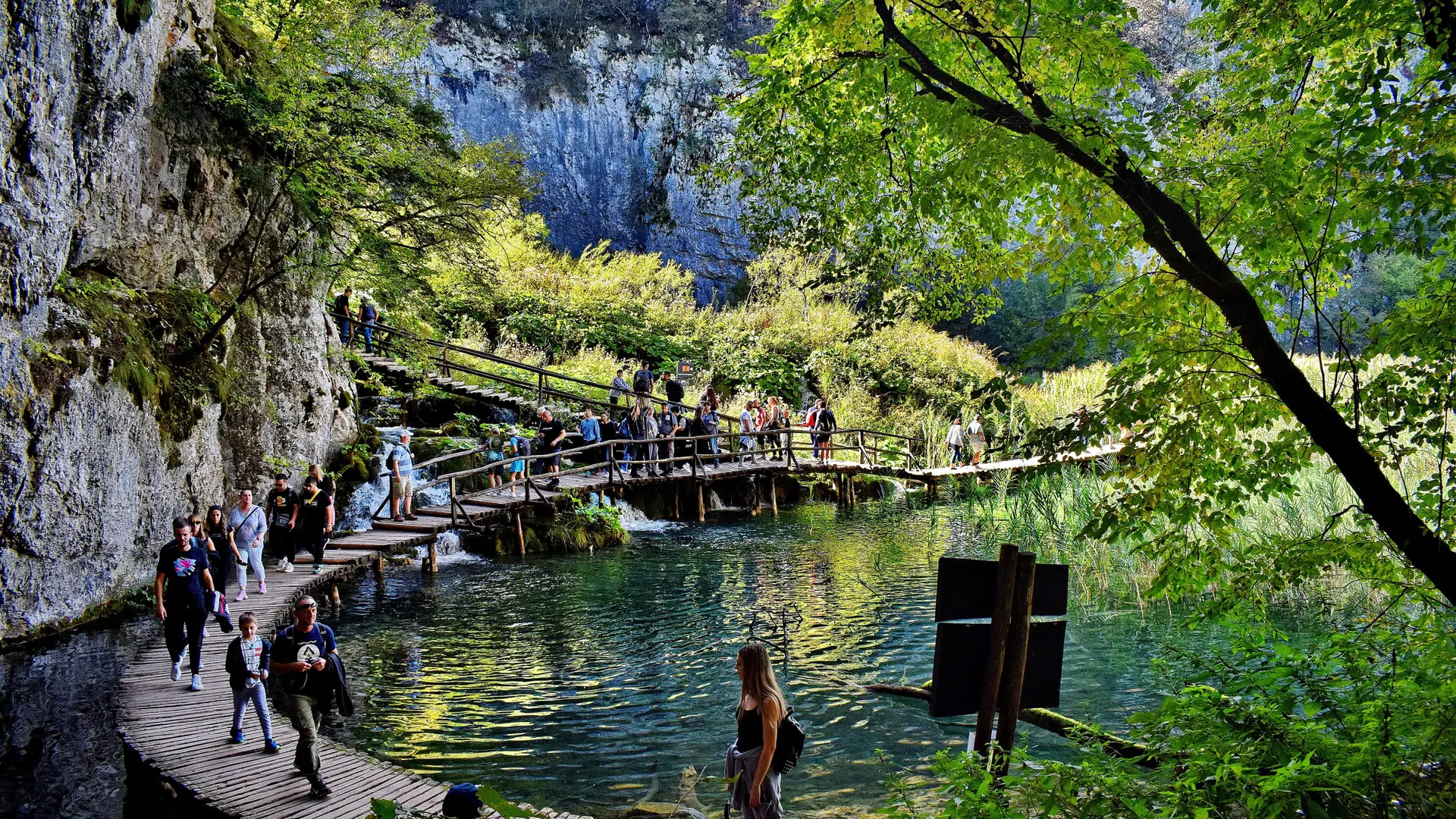 Wooden boardwalk beside turquoise water and forest waterfalls at Plitvice Lakes