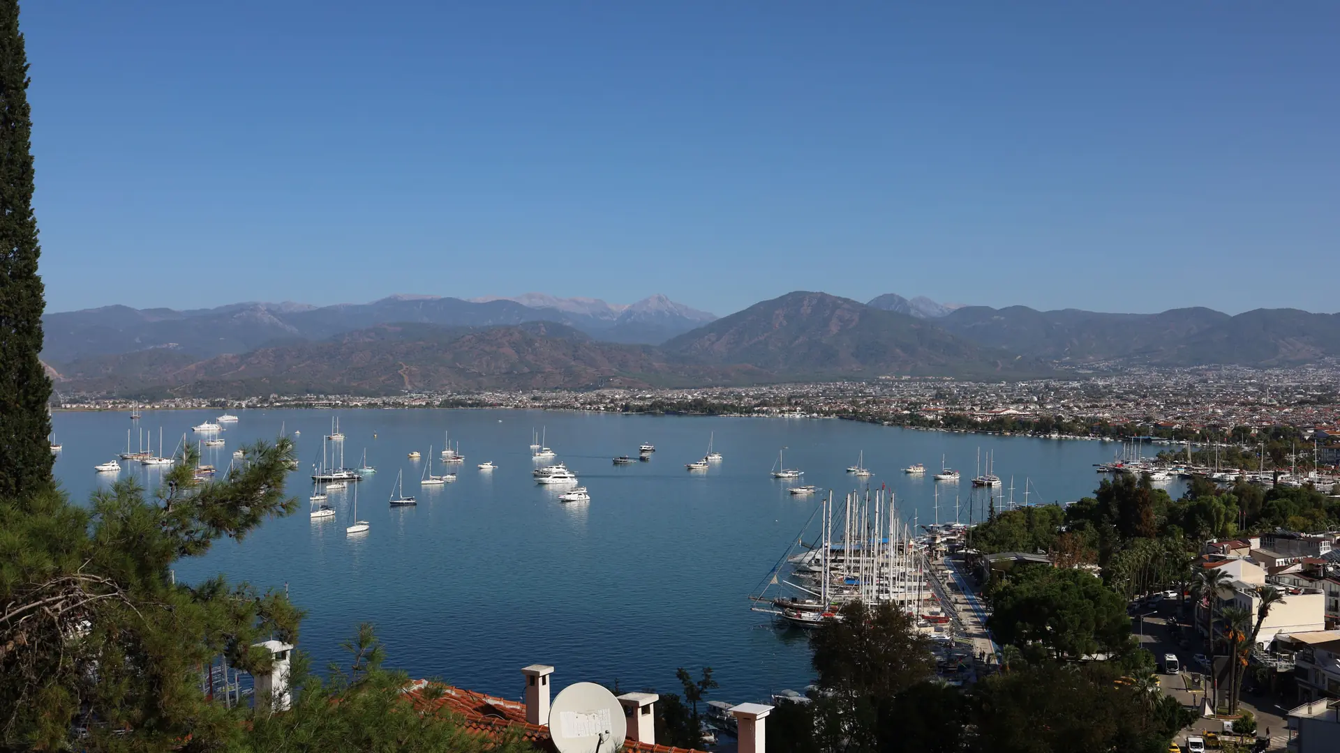 Fethiye marina and bay with sailing yachts, red-roofed town buildings and distant mountain ridges