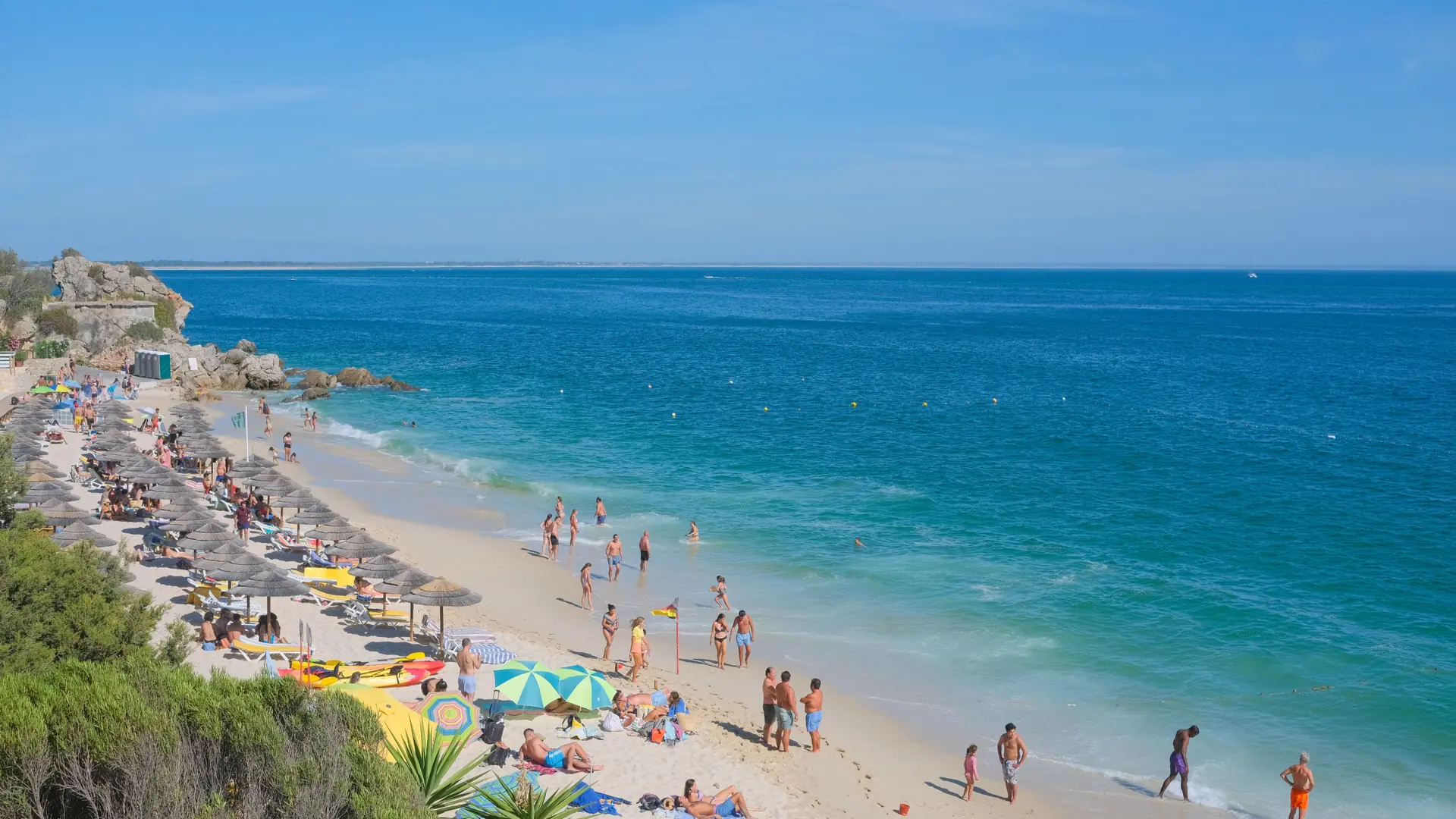 vivid turquoise water and thatched sunbed umbrellas along Praia da Oura in Albufeira