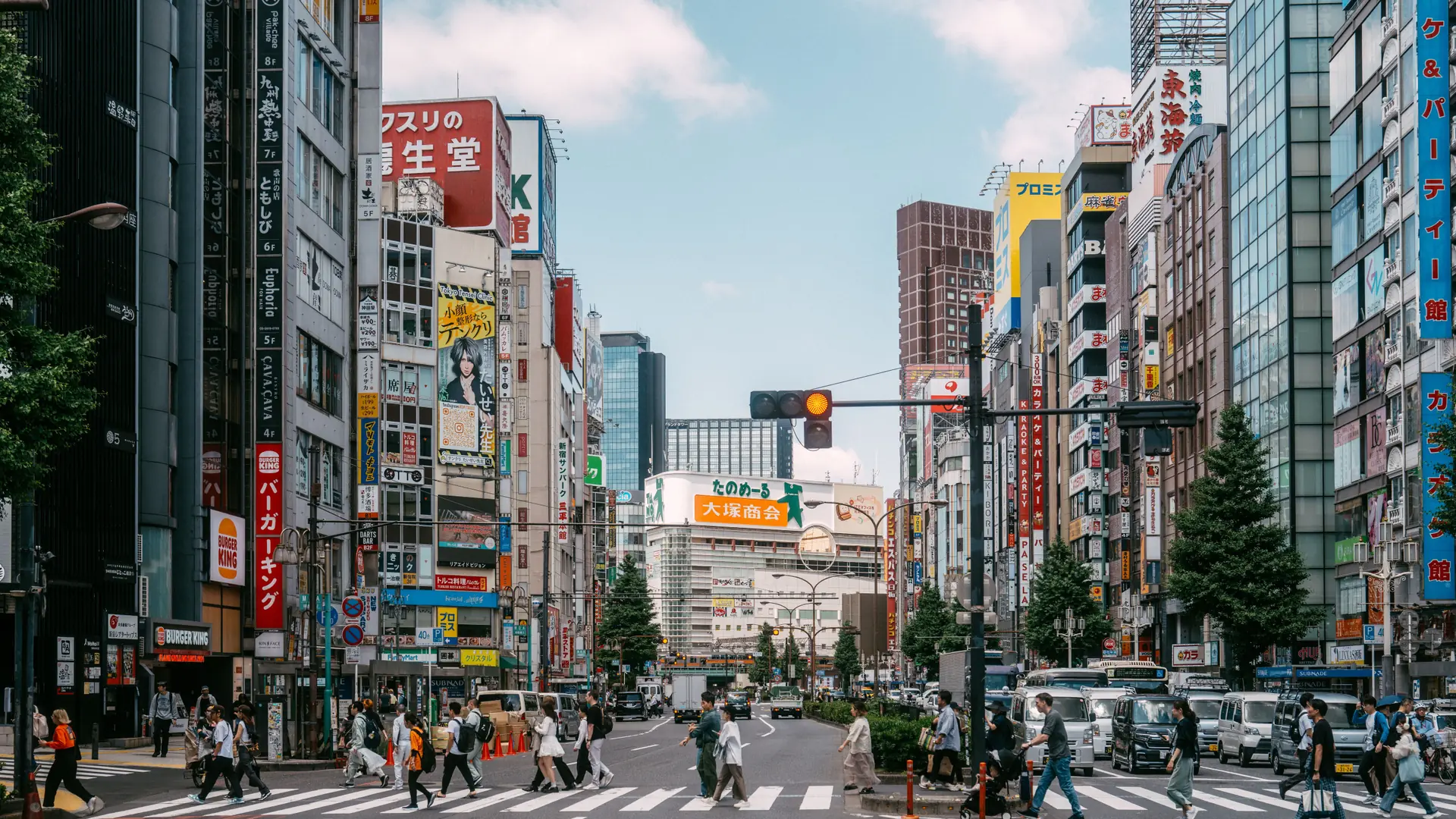A broad Shinjuku avenue lined with colourful signs and busy crossings in daylight