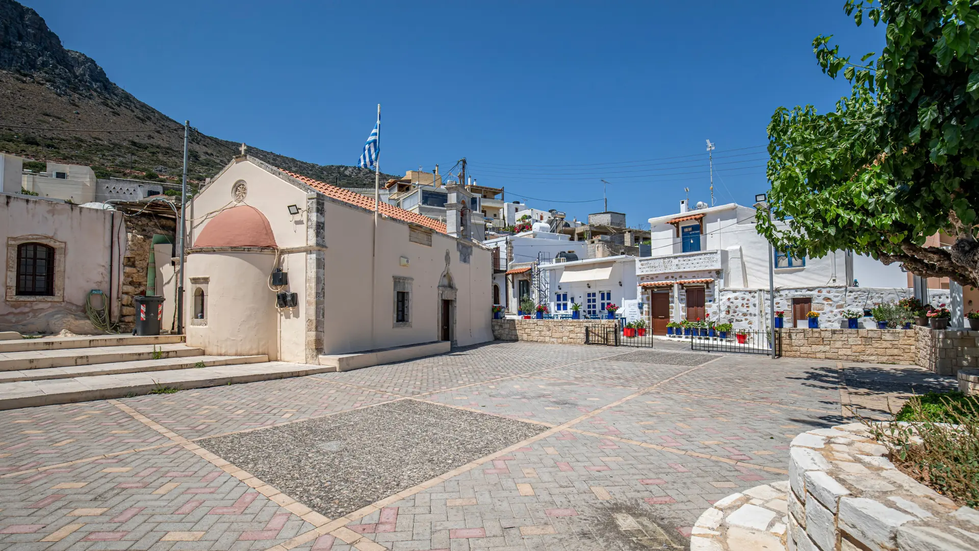 A quiet paved square with stone buildings and a white church in sunny Areopoli