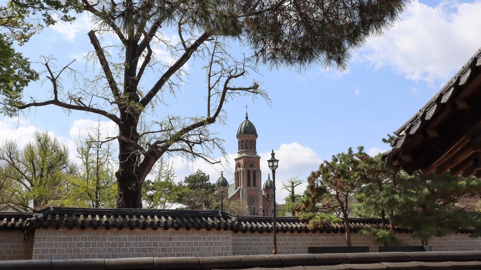 Jeondong Catholic Cathedral's domed brick towers rising behind a traditional Jeonju hanok wall, in bright daylight