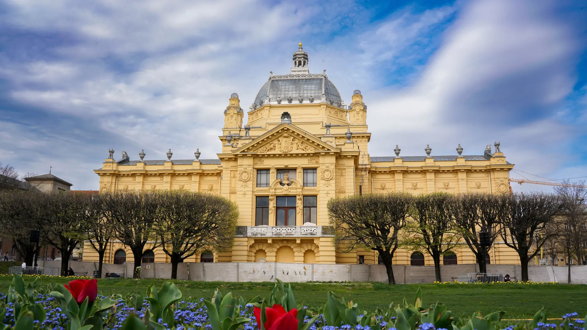 The yellow Art Pavilion behind spring flowers in Zagreb’s Lower Town