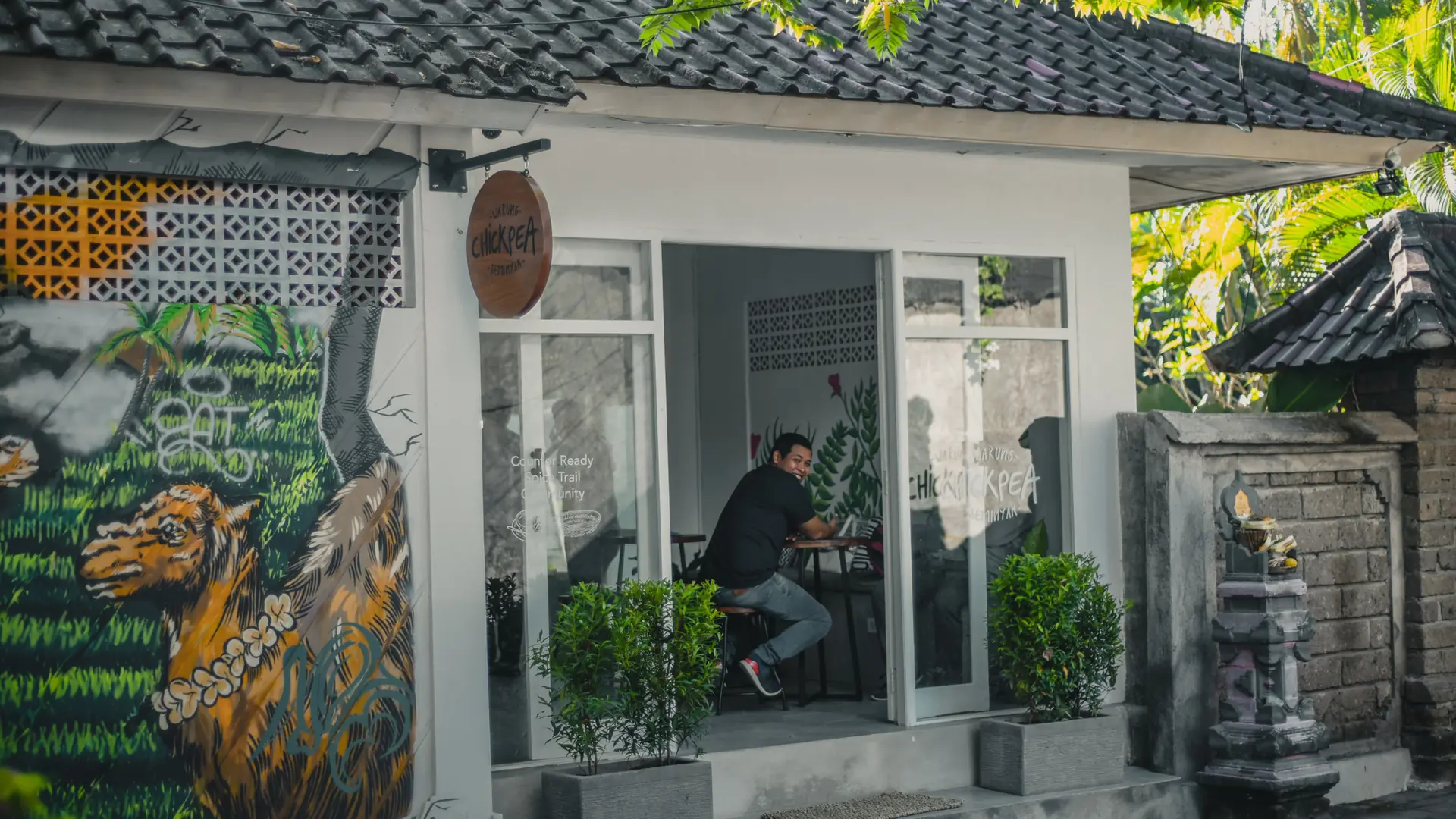 A small Bali café with outdoor seating, tropical plants and a colourful tiger mural