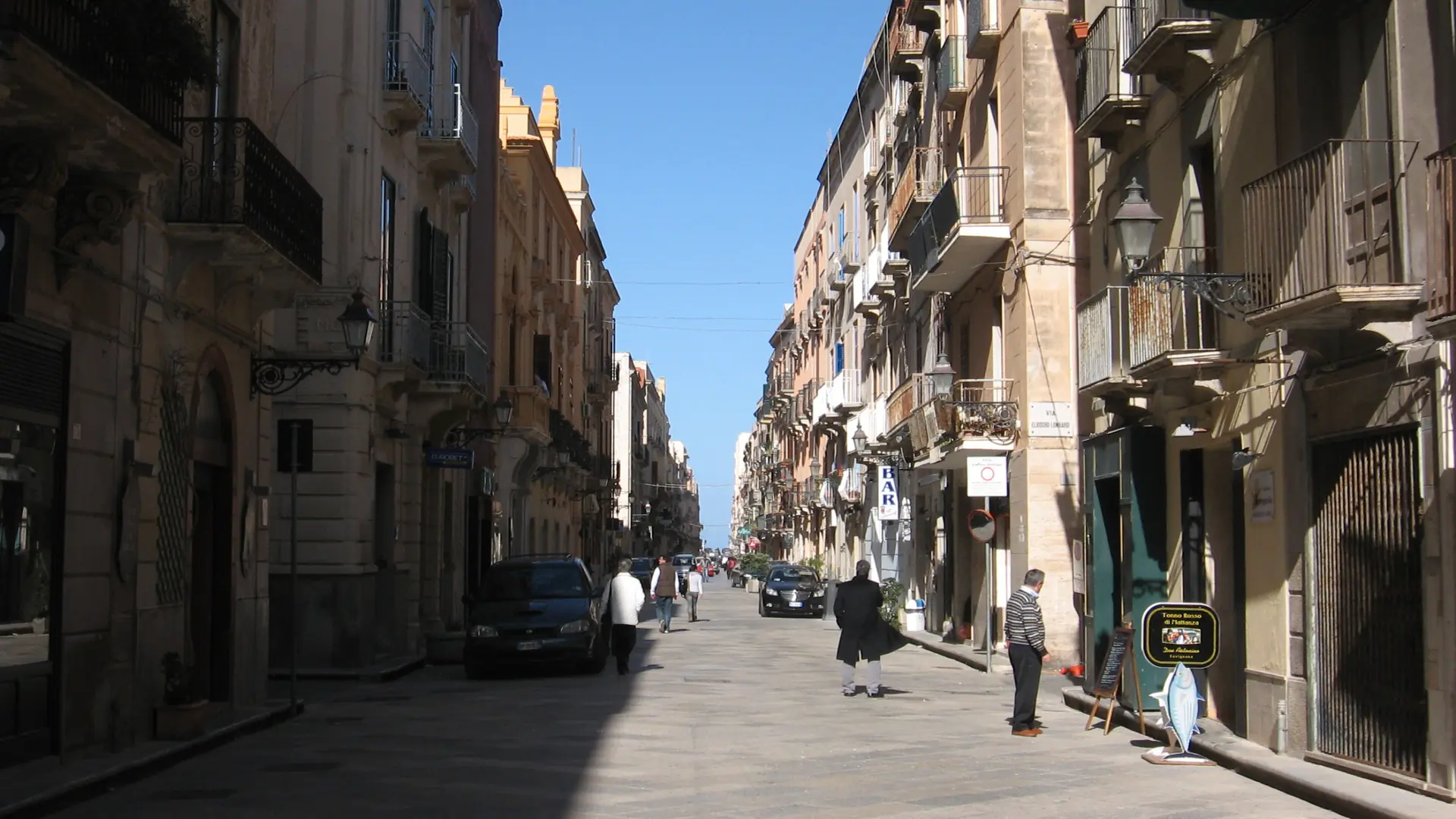People walking along Corso Vittorio Emanuele in Trapani between balconies and sunlit façades.
