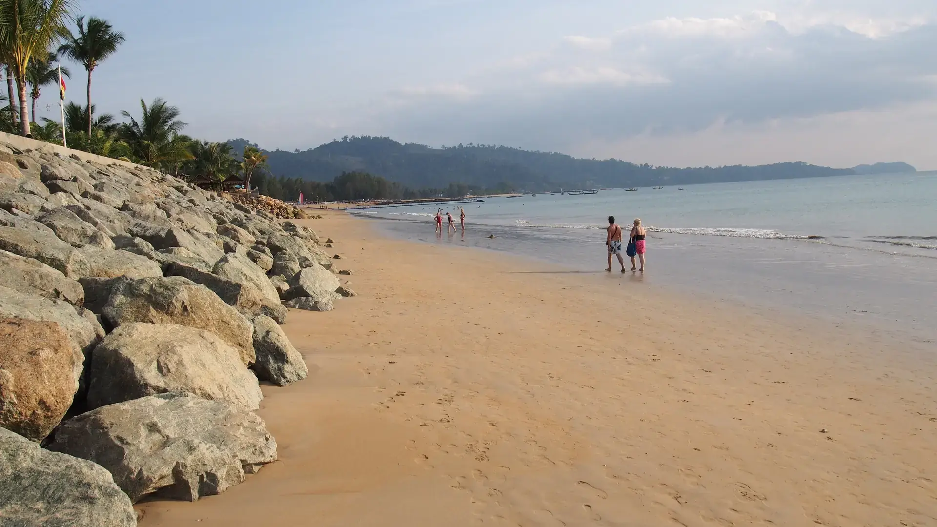 A broad Khao Lak beach edged by palms and low green hills