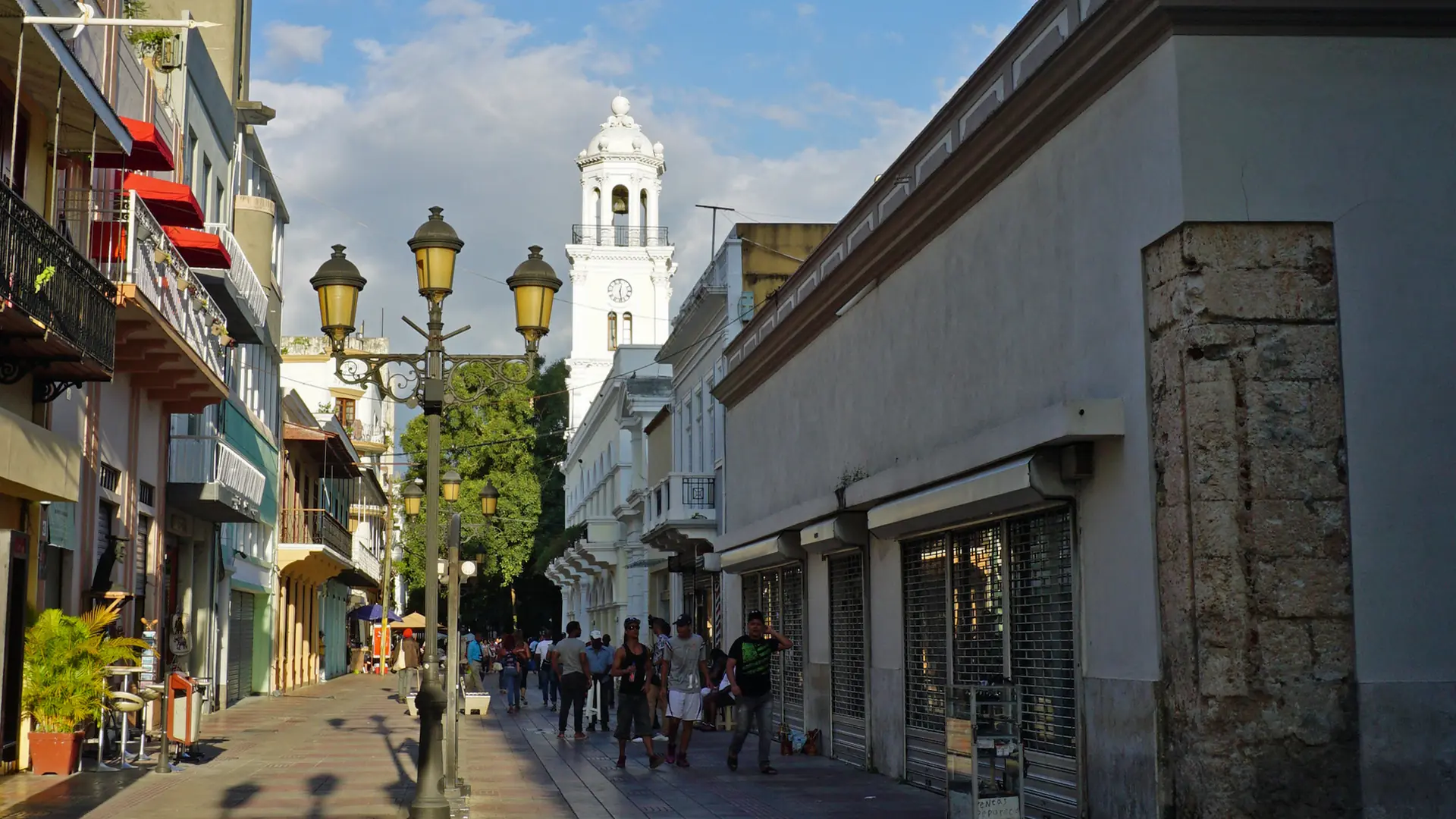 Sunlit Calle El Conde with old facades and a distant church tower in Santo Domingo
