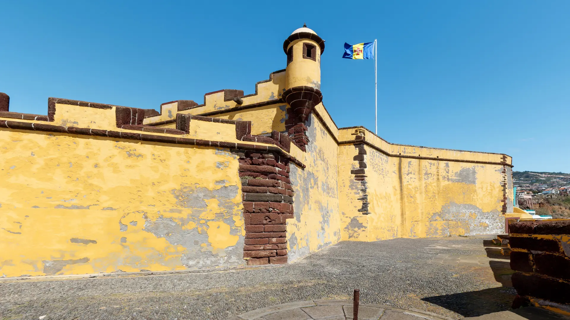 Yellow walls and a turret of São Tiago Fort beside Funchal’s Zona Velha under a blue sky