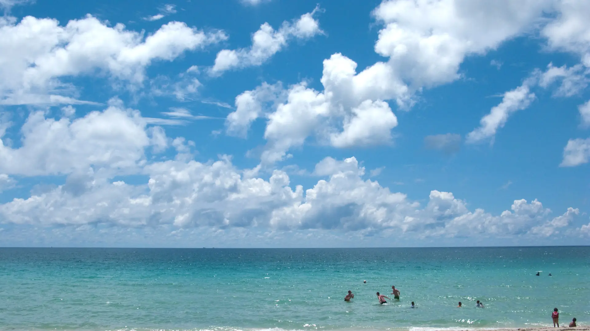 White Koh Samui beach meeting bright blue Gulf water under high clouds