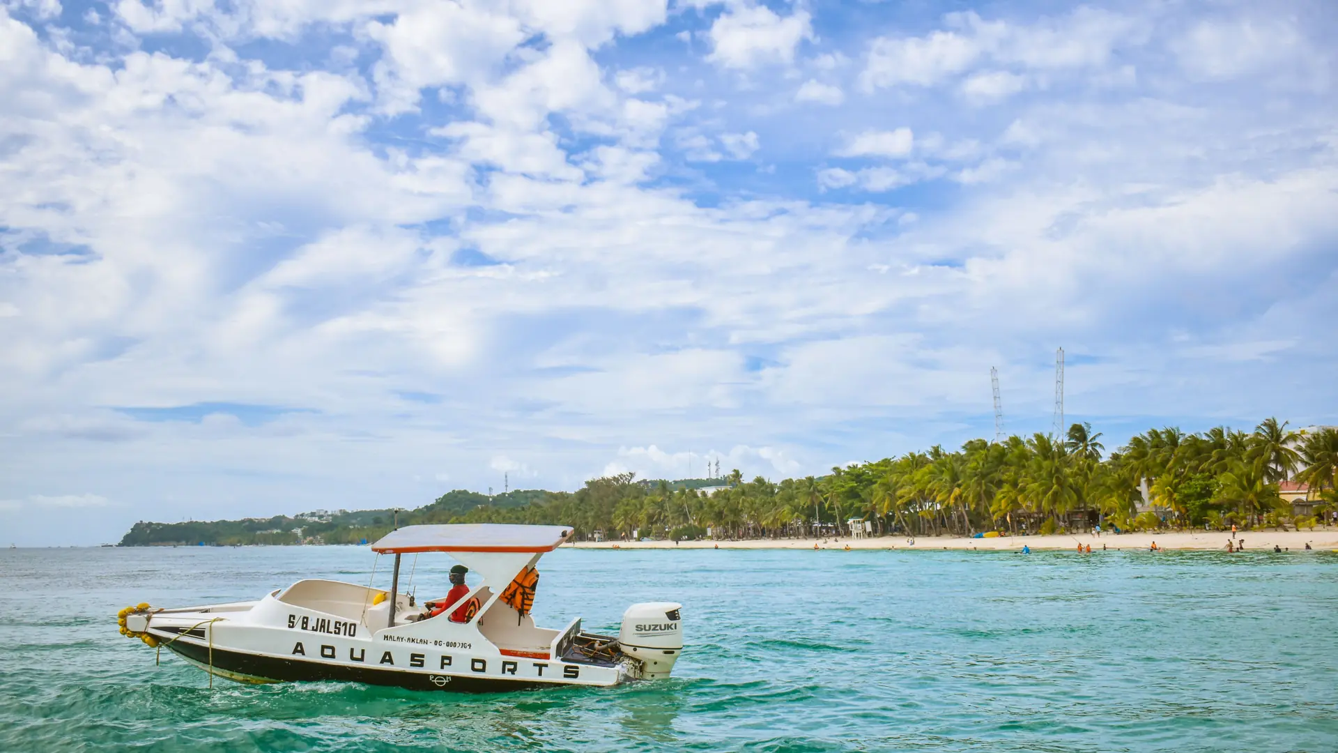 A motorboat on blue water beside Boracay’s white-sand shore and palms in daylight