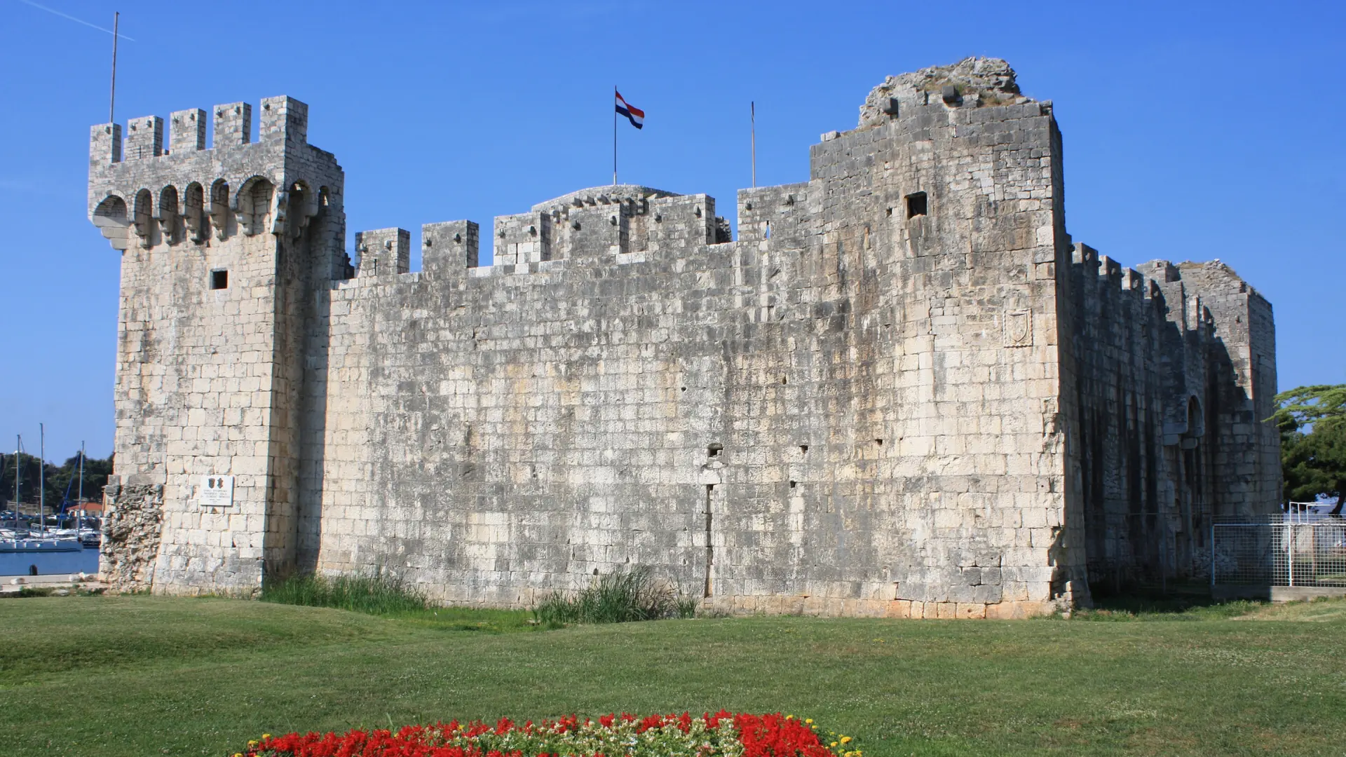 The stone walls and towers of Kamerlengo Fortress beside a grass lawn in Trogir