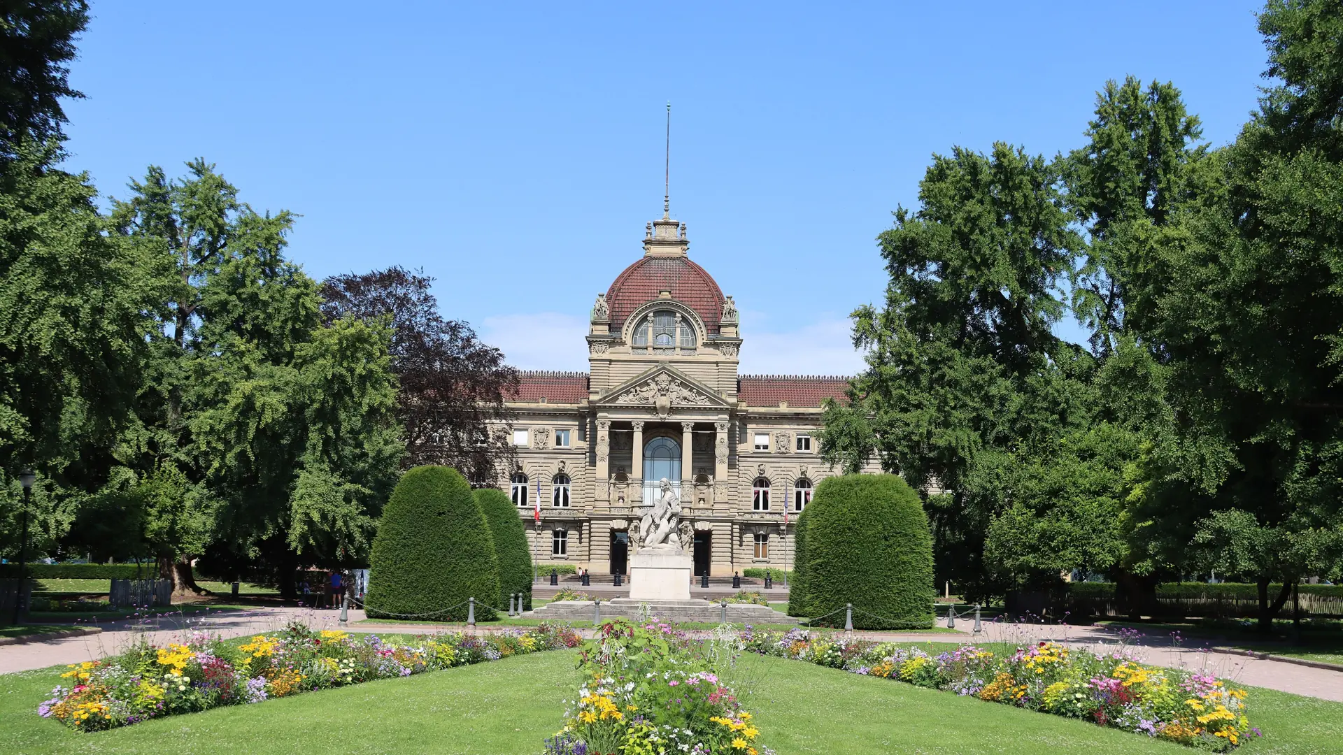 The Palais du Rhin beyond sunlit flowers and lawns in Strasbourg’s Neustadt