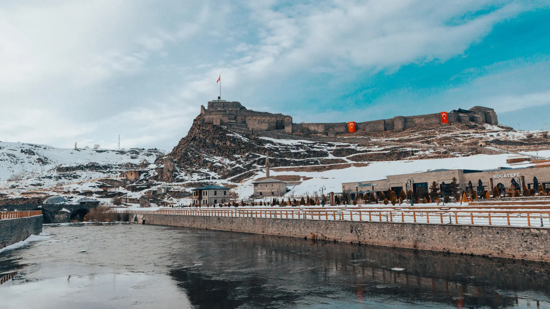 Snow-covered Kars Fortress and river beneath Turkish flags