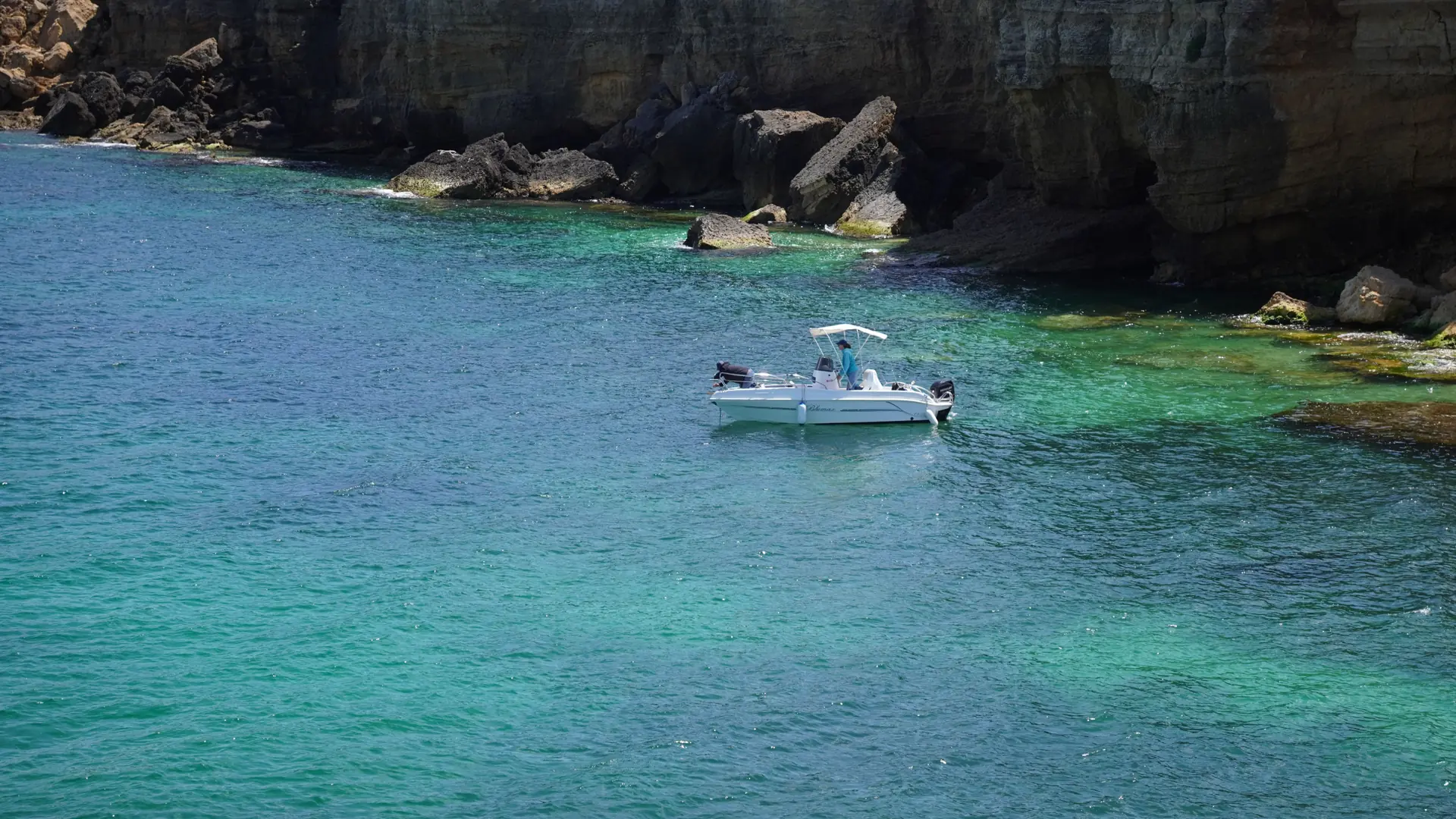 a small boat on vivid turquoise water beneath sandstone cliffs near São Rafael, Albufeira