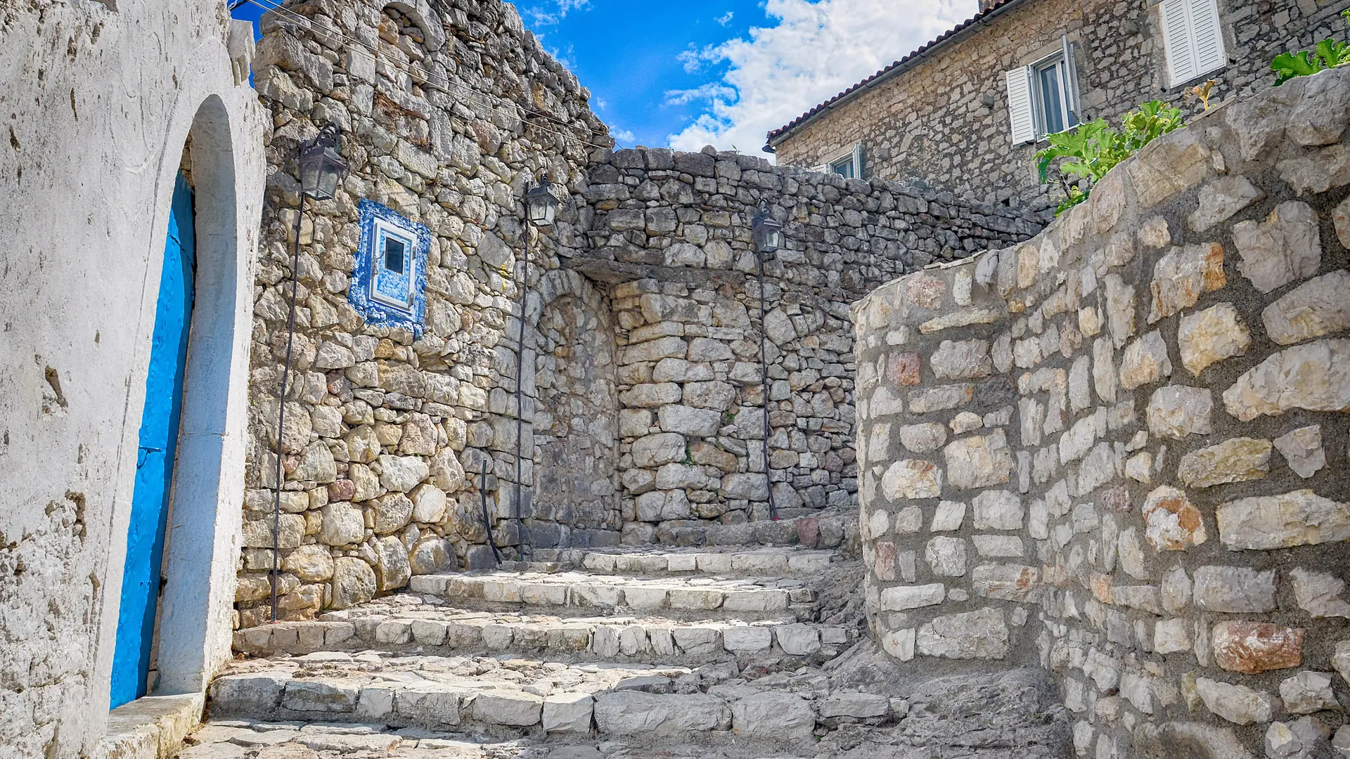 A stone lane and steps between old houses inside the castle district of Old Himarë under a blue sky
