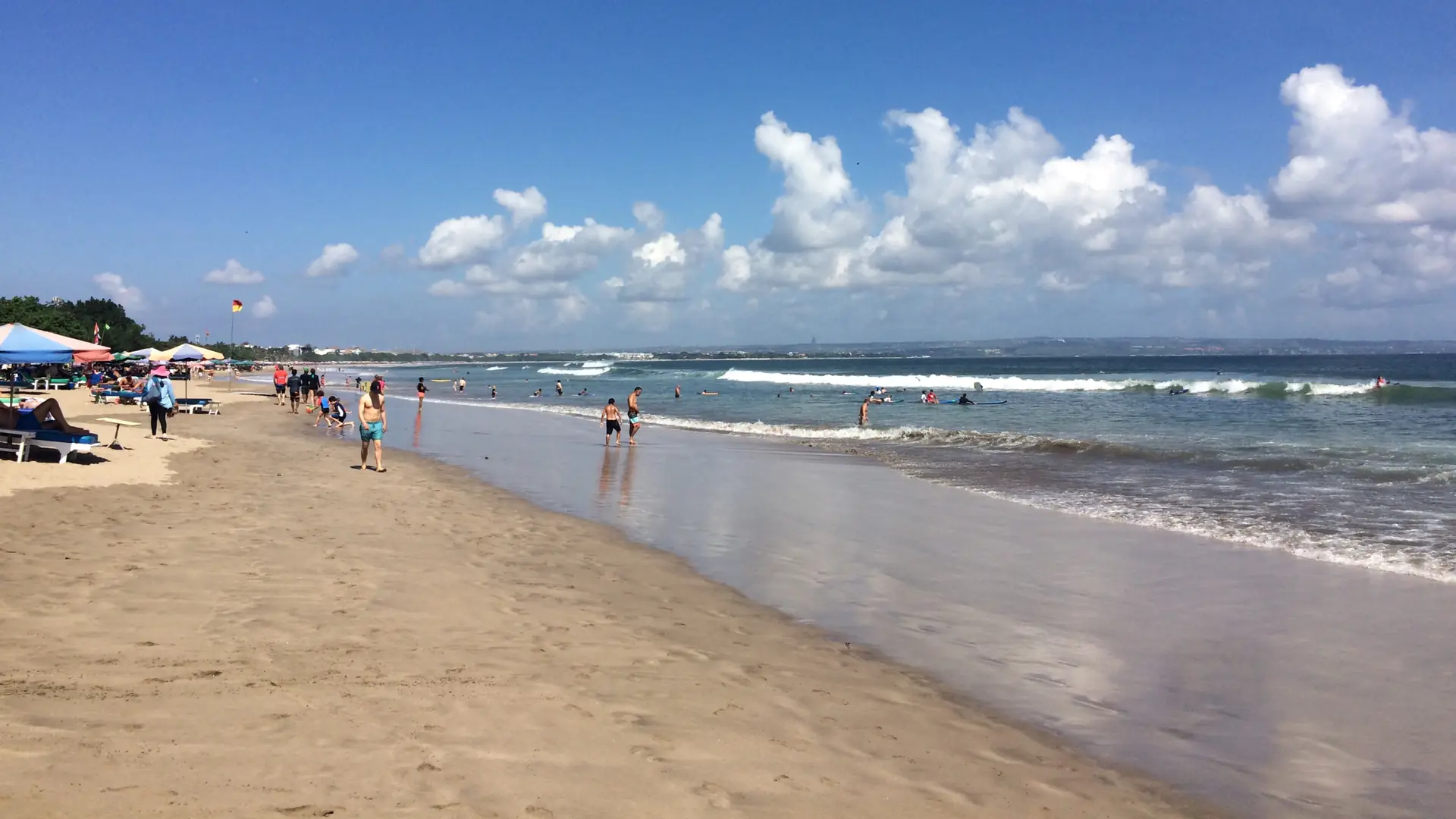 People beside ocean surf on a sunny west-coast beach in Kuta, Bali