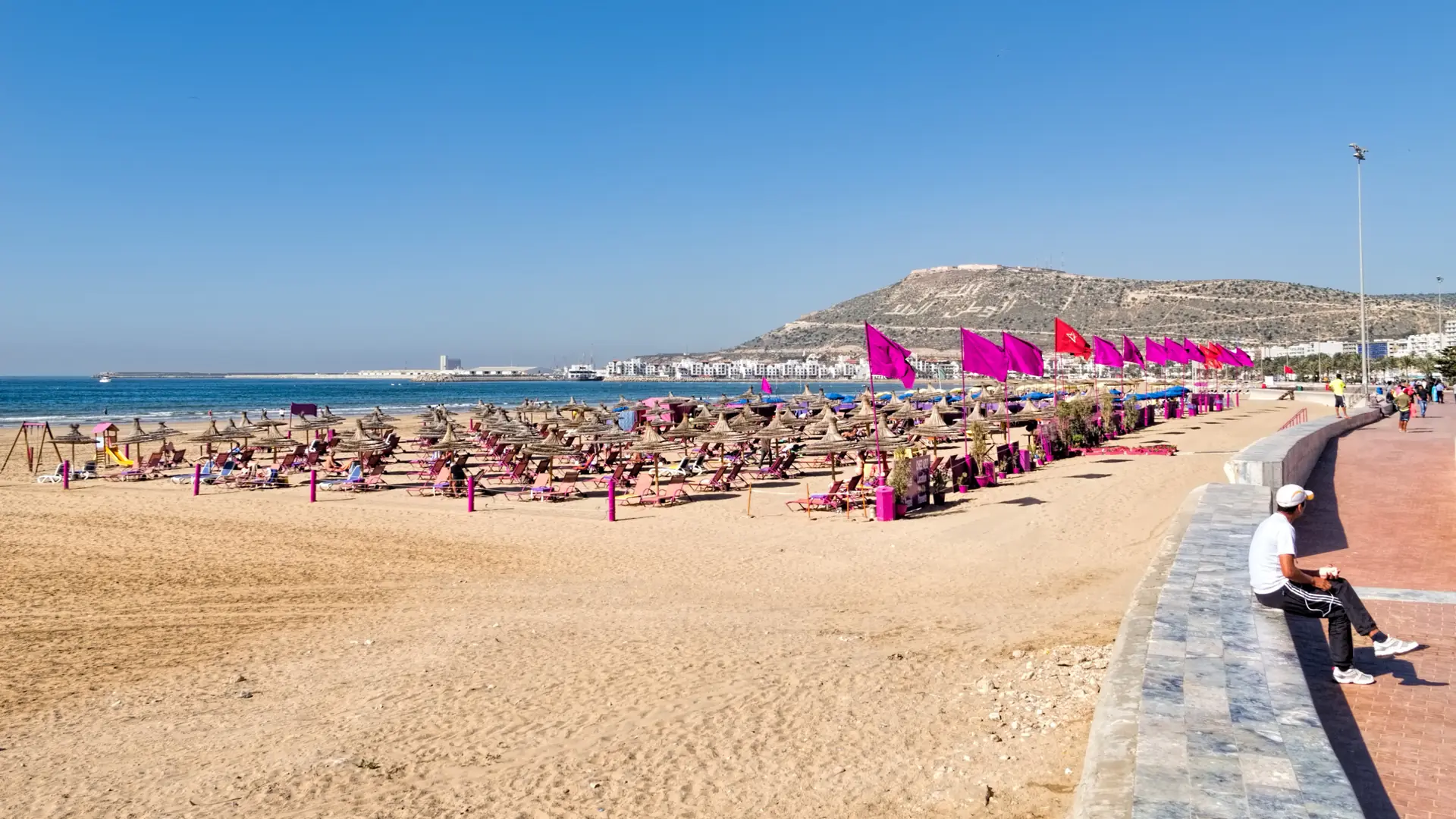 Sunny Agadir beach with bright parasols, blue Atlantic water and Kasbah hill behind
