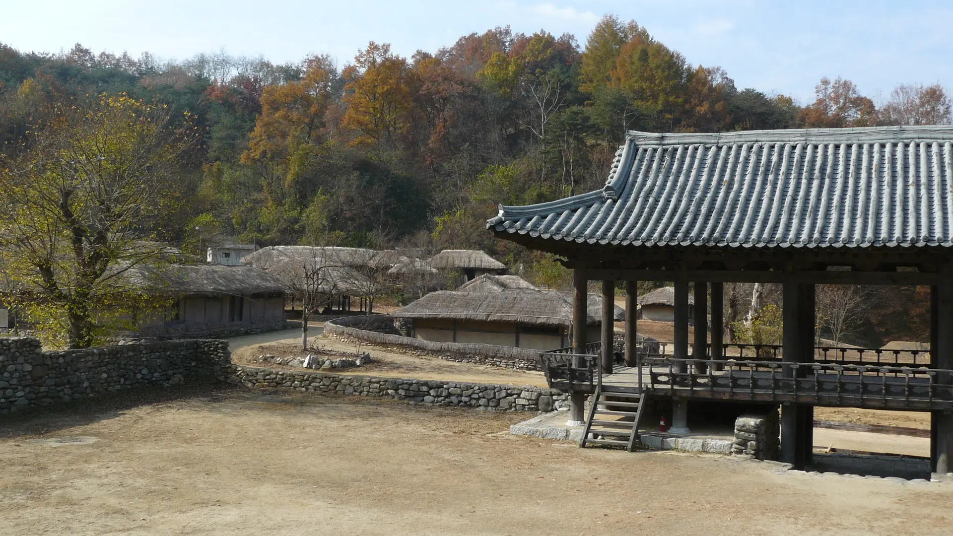 A tiled-roof wooden pavilion at Hahoe Folk Village, with a courtyard and trees behind it, Andong