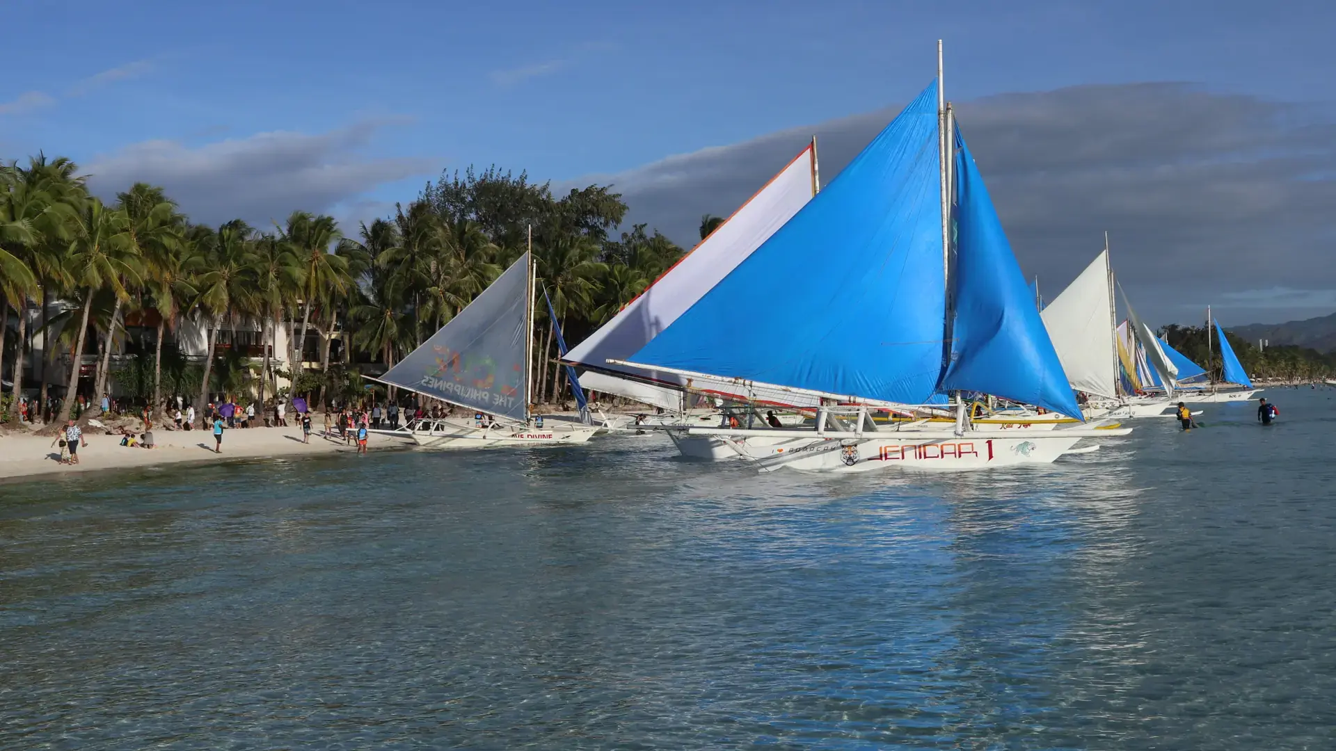 Paraw sailboats with blue sails moored off the palm-lined sand of Station 2, Boracay