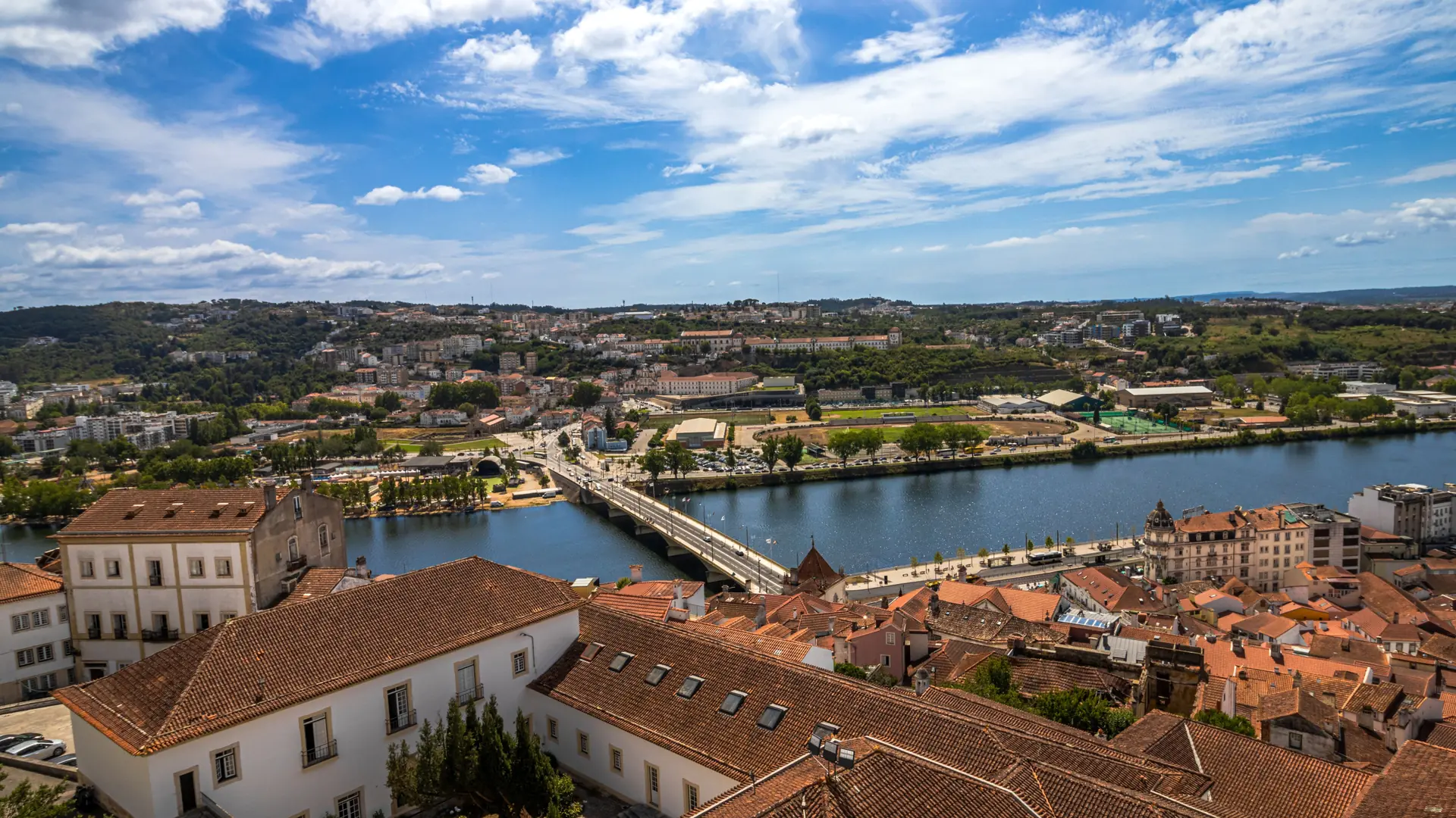 Aerial view across Coimbra’s red roofs and the Mondego River beneath a blue sky