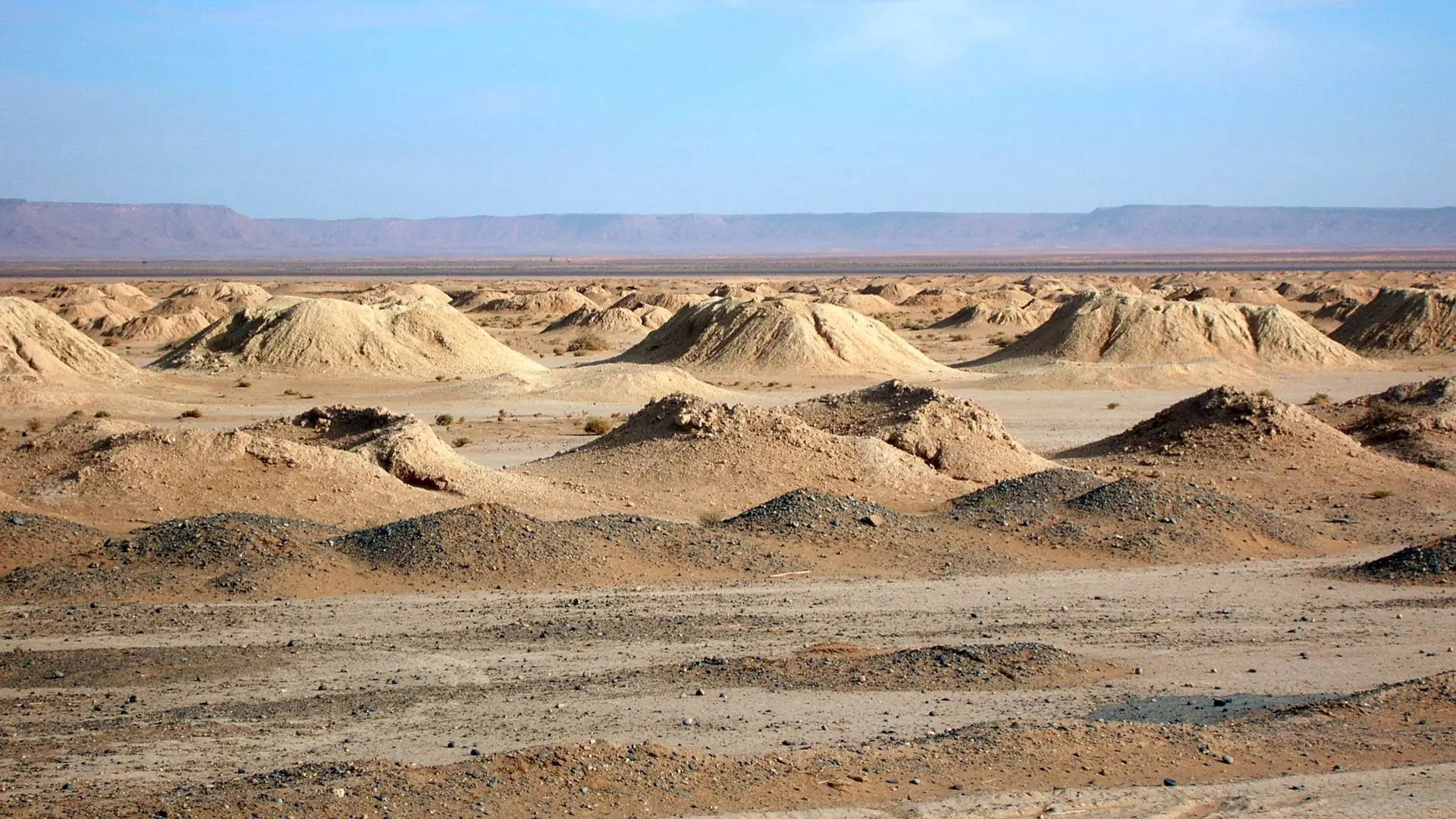 Khettara earth mounds across the bright desert plain near Erfoud