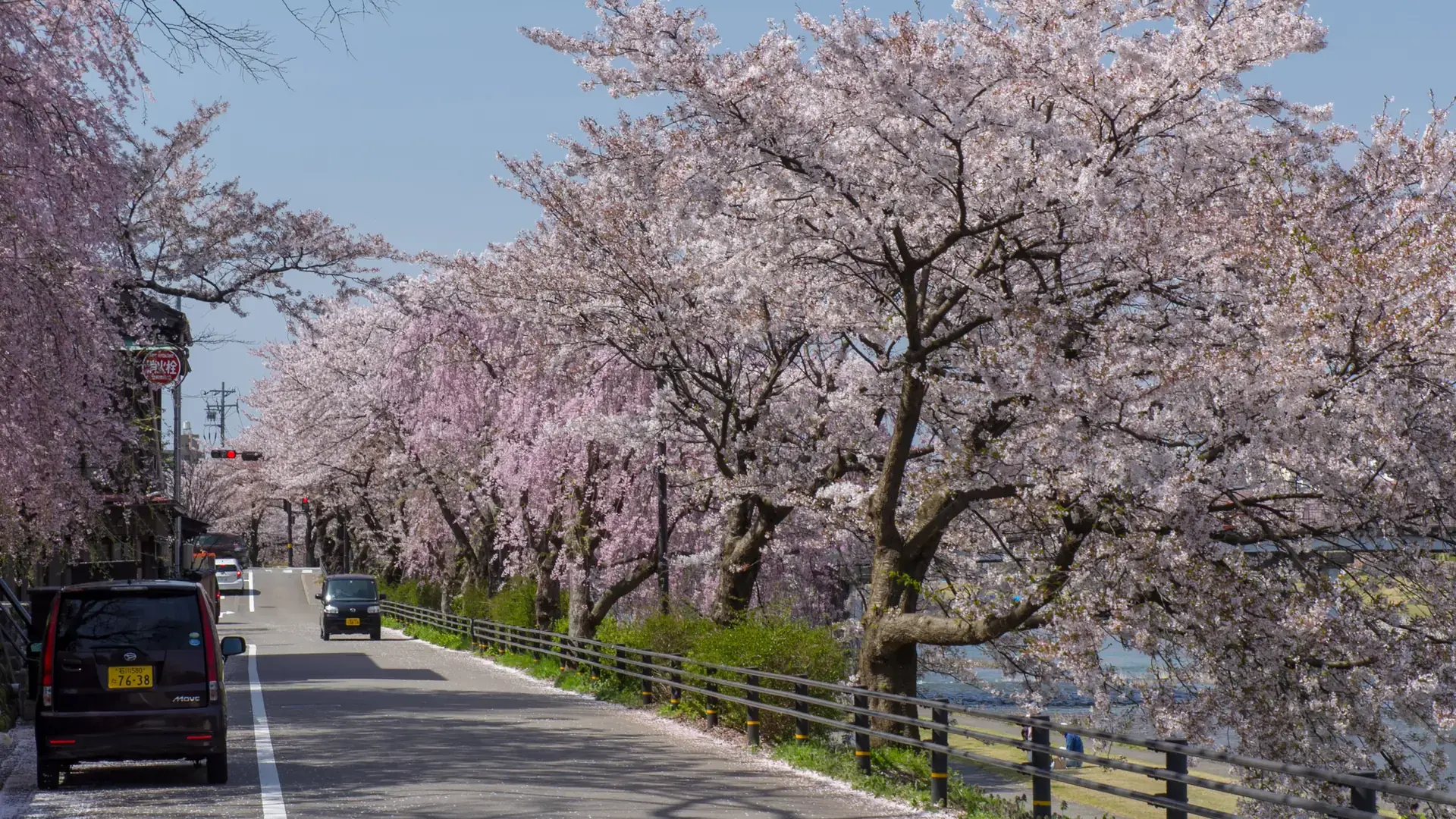 sunlit Sai River promenade with Kanazawa hills and blue water beyond