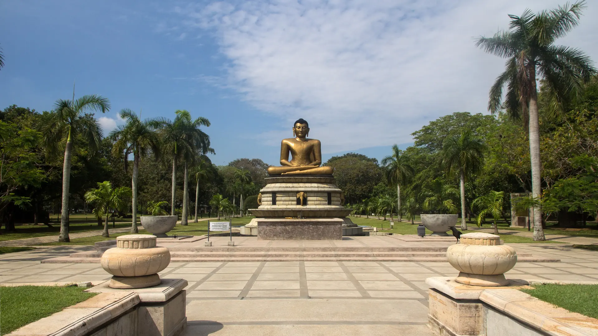 Seated golden Buddha statue among palms in Viharamahadevi Park, Colombo