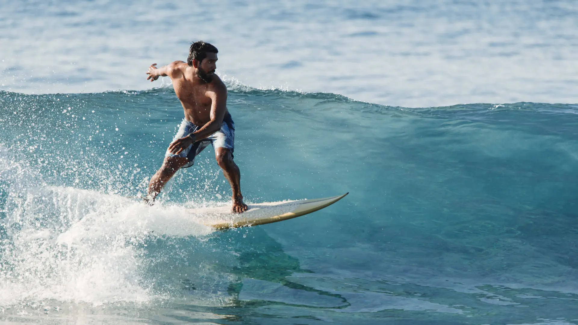 Surfer riding a turquoise wave in the Maldives