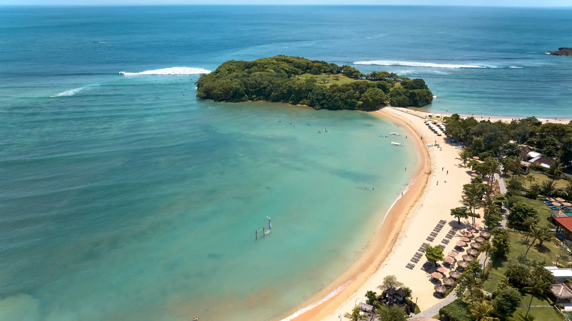 An aerial view of Nusa Dua’s curved sandy beach and turquoise water beside a green headland