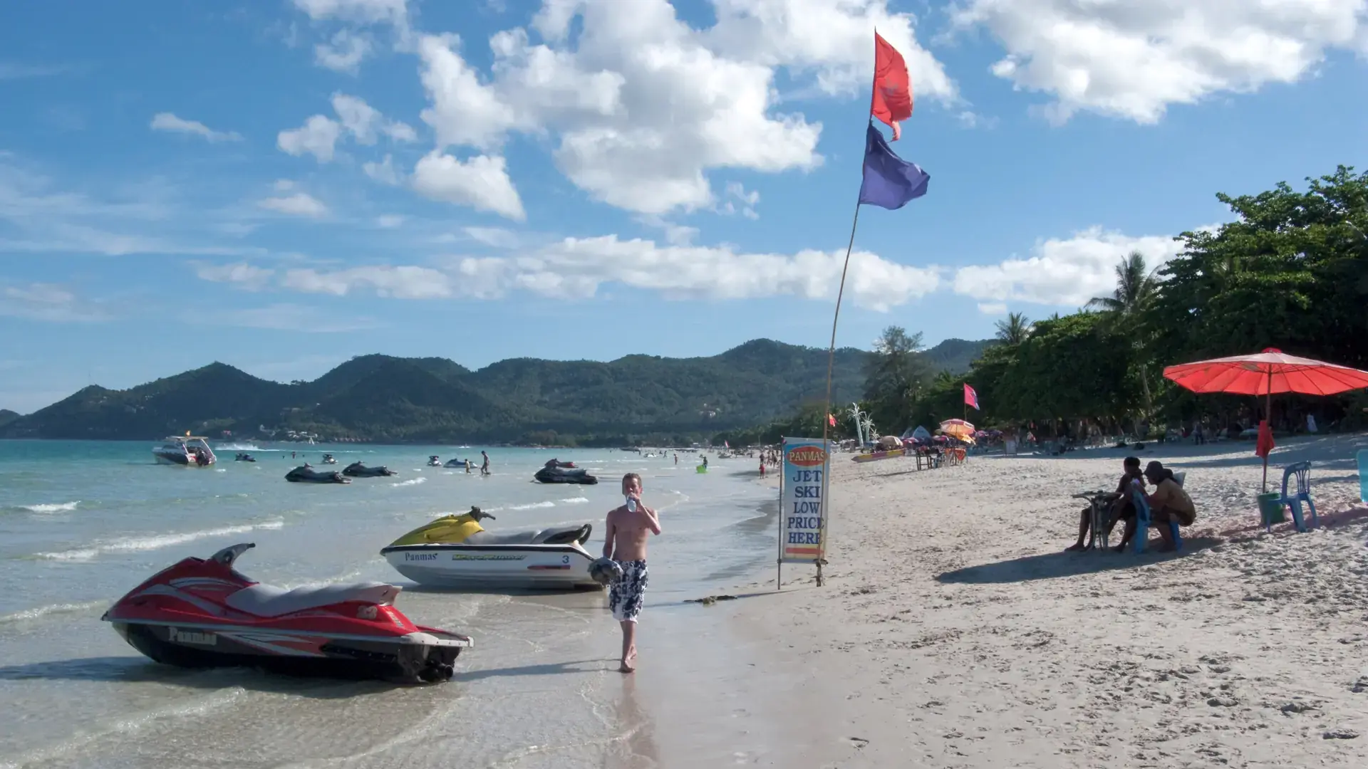Sunny Koh Samui beach with forested hills, parasols and jet skis; a wider-island scene, not Nathon waterfront
