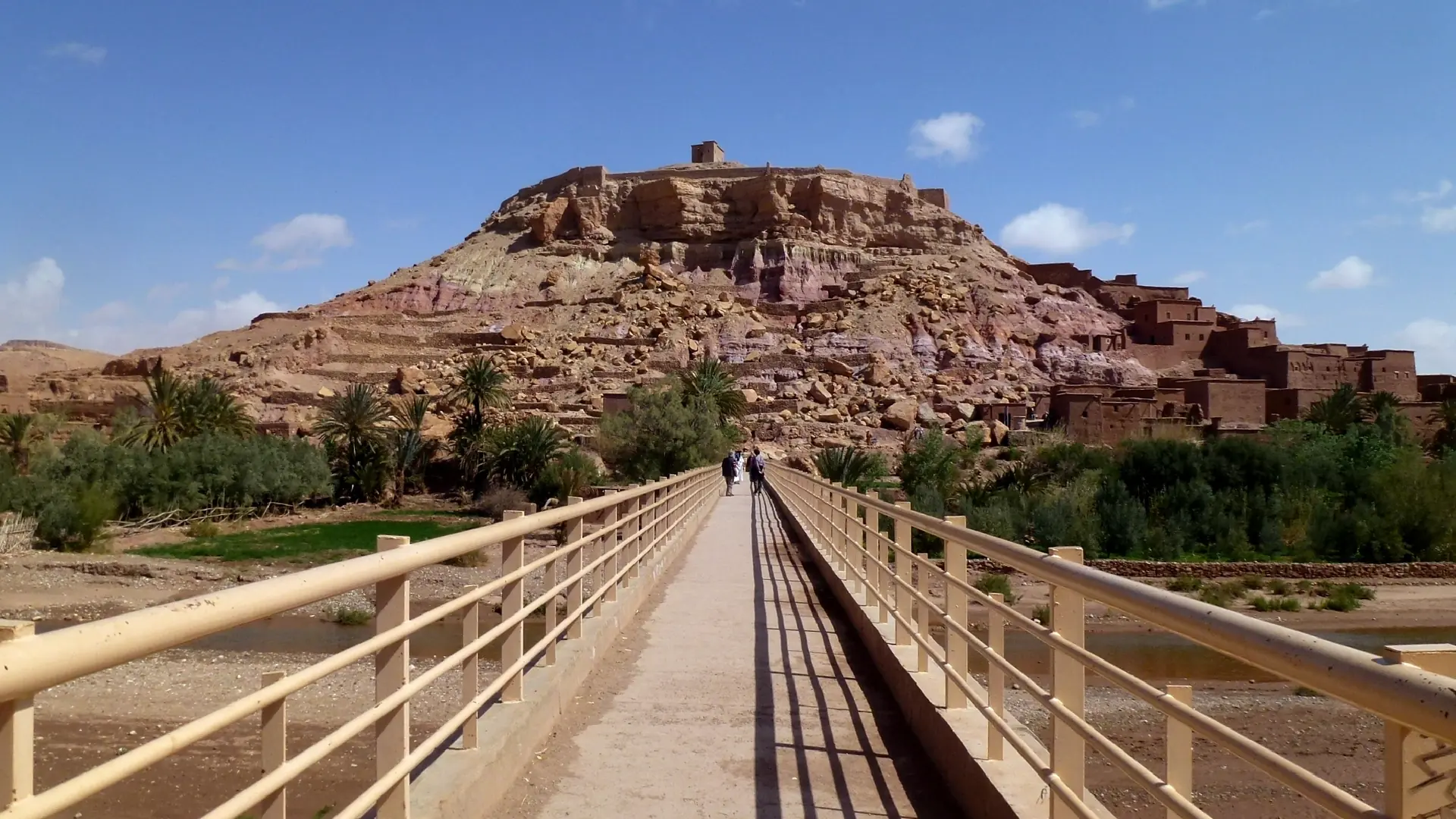 Footbridge leading toward the earthen ksar of Ait Ben Haddou beneath a sunny sky
