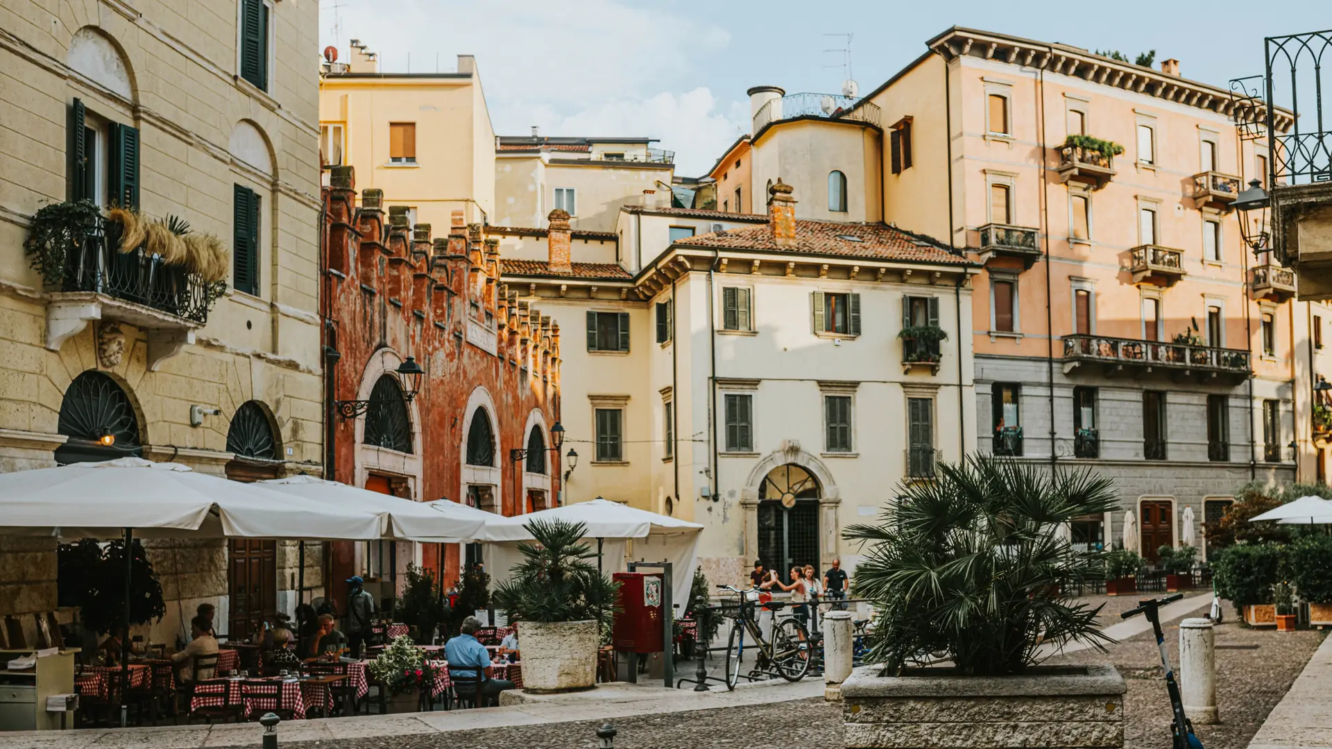 a sunlit Verona piazza with café terraces and warm-toned historic façades