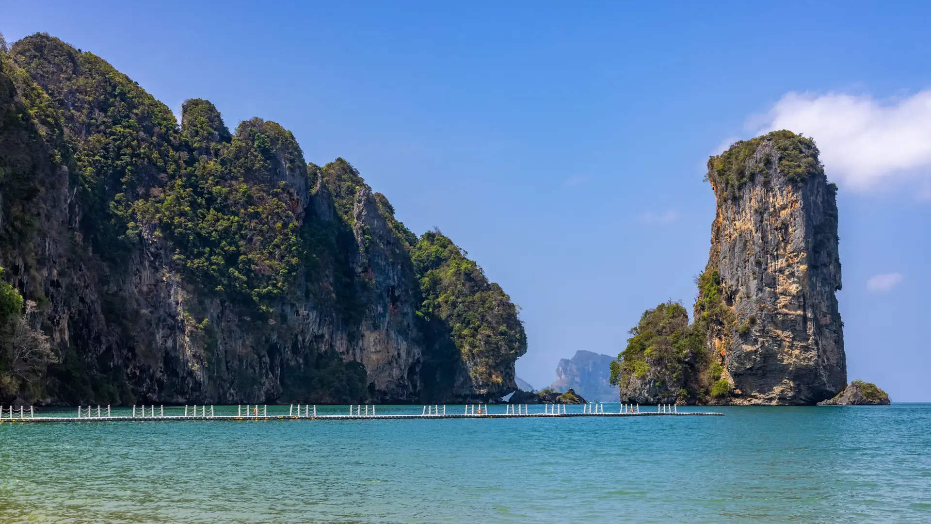A floating walkway and sunlit limestone formations along the Krabi coast