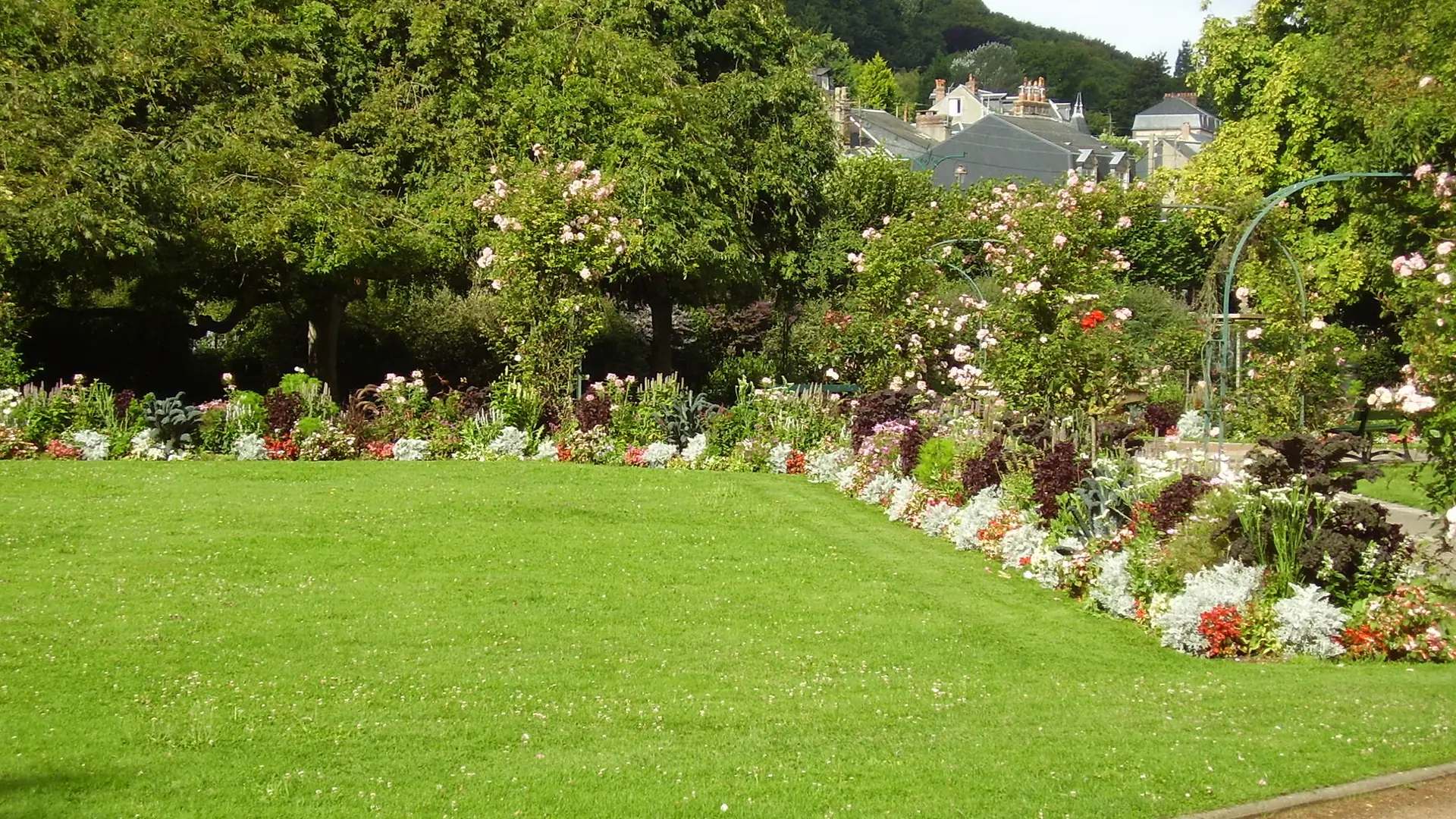 Flower beds, rose arches and a lawn in a public garden in Honfleur