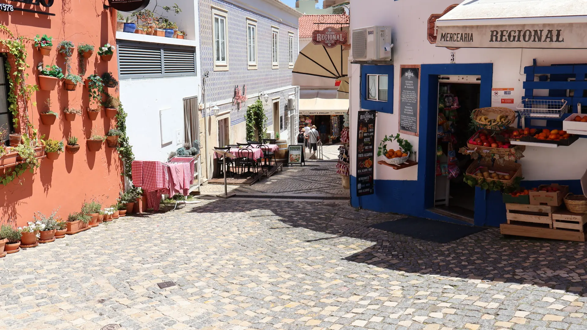 a sunlit cobbled pedestrian street in Lagos old town with shopfronts and café tables