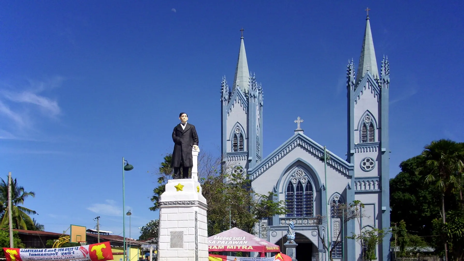 The Rizal monument in front of the twin-spired Immaculate Conception Cathedral in Puerto Princesa under a blue sky